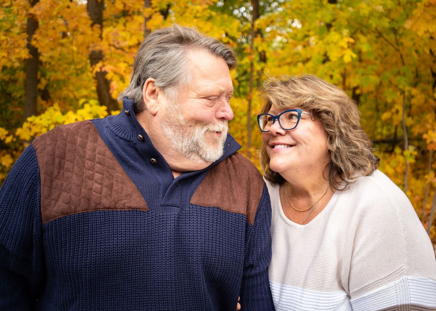 Couple laughing together in autumn park with golden foliage in background.