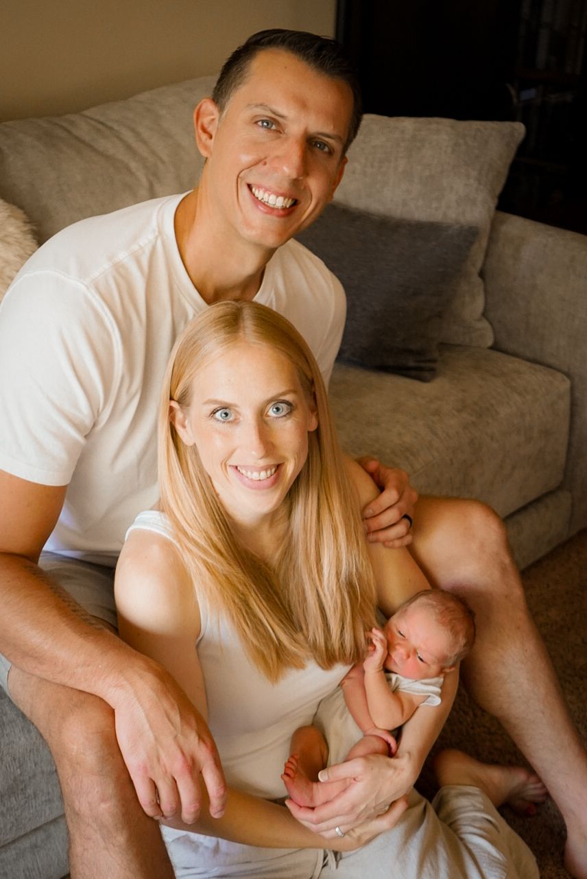 Candid family moment with parents cuddling newborn on grey sofa.