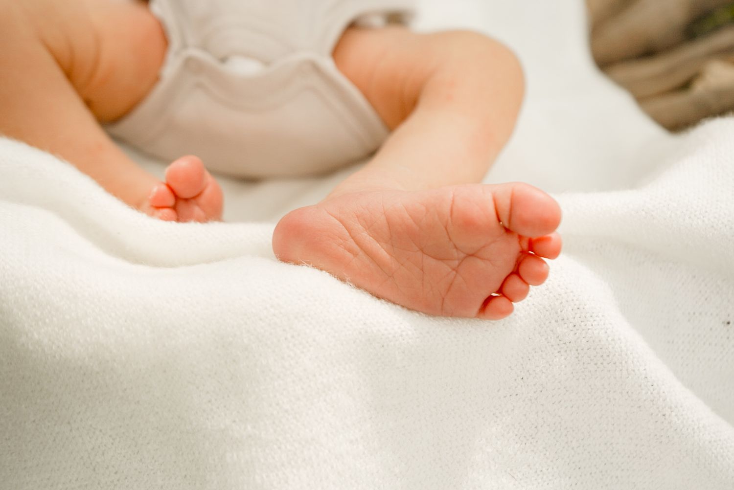 Tender massage movements shown on a newborn's tiny feet and legs against white fabric.