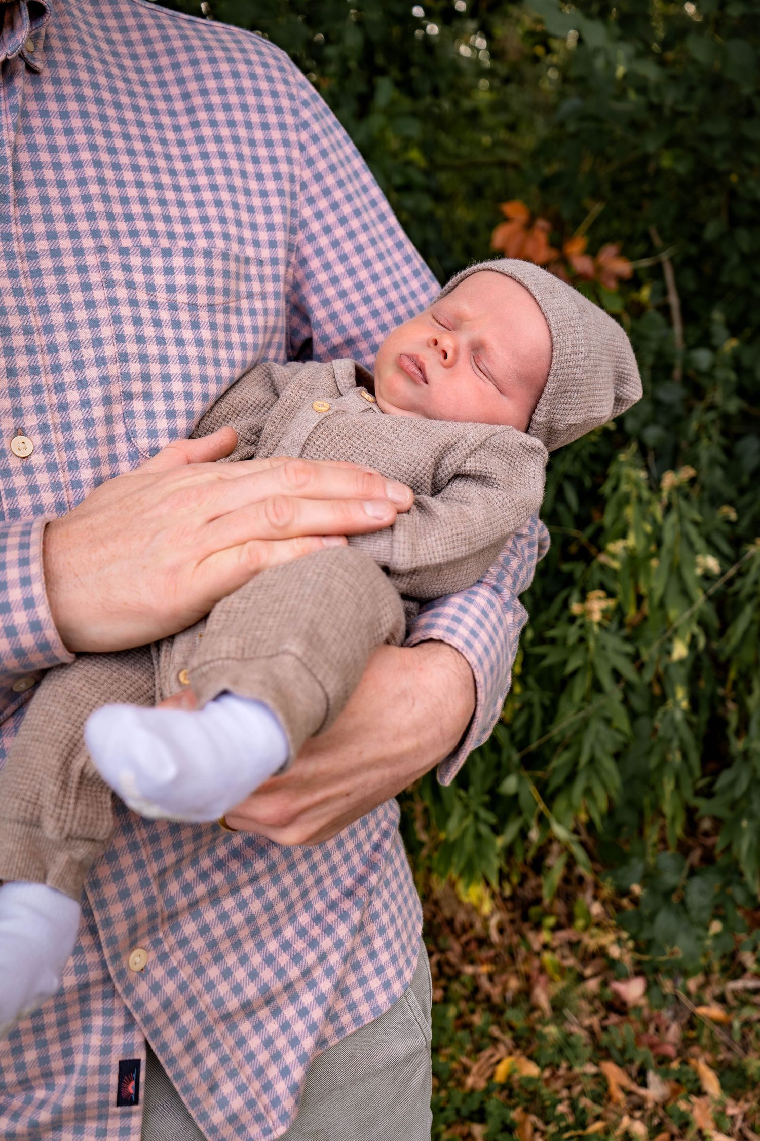 Baby in grey sweater being cradled during outdoor autumn family photoshoot.