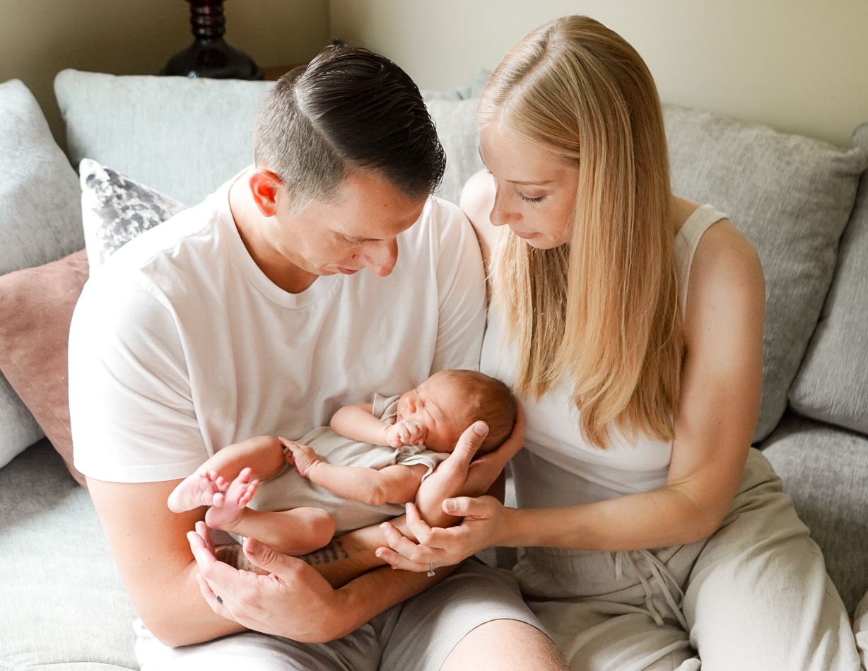 Parents lying on couch sharing intimate moments with their newborn baby.