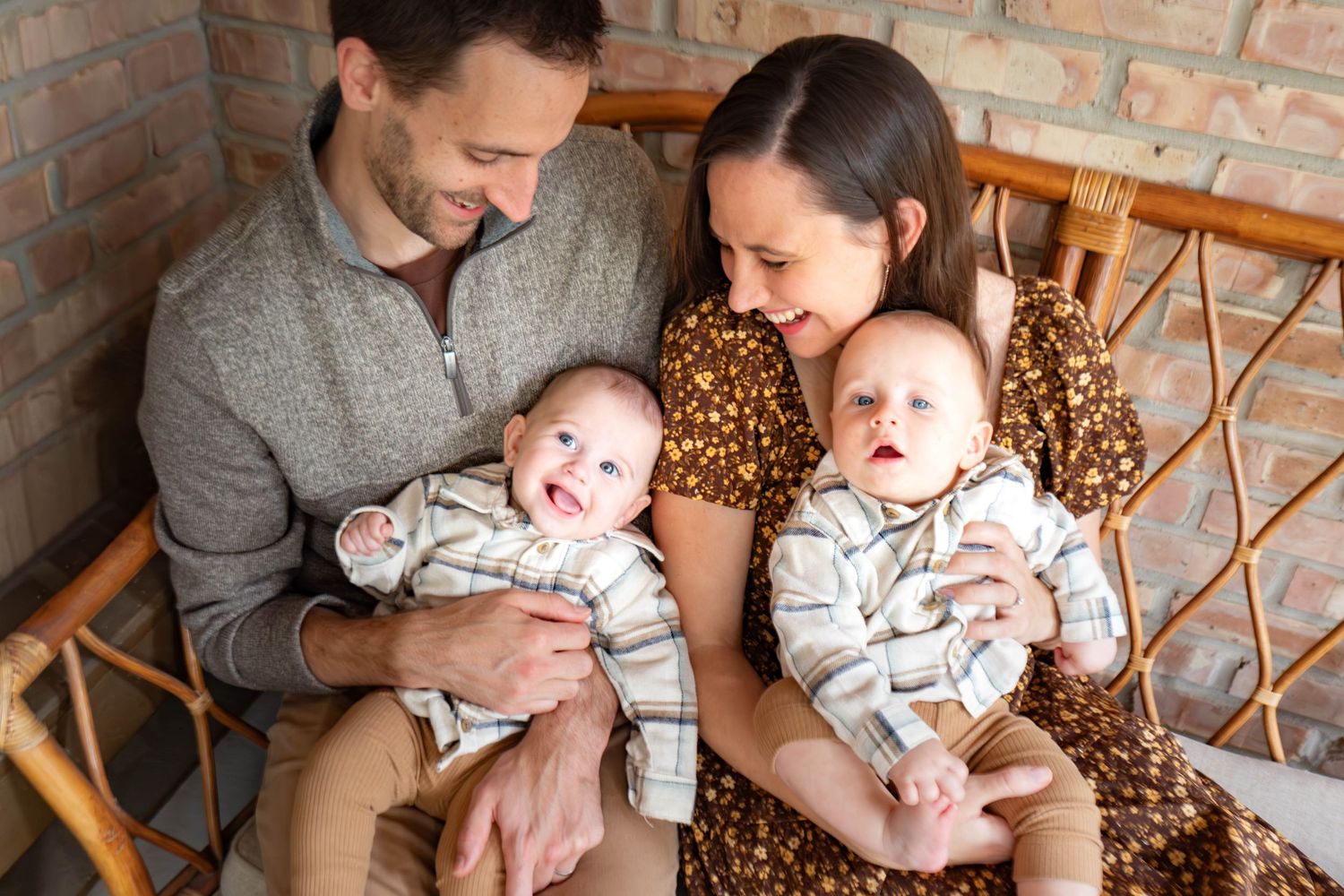 A couple sits on a wooden bench while holding twin babies dressed in matching striped outfits.