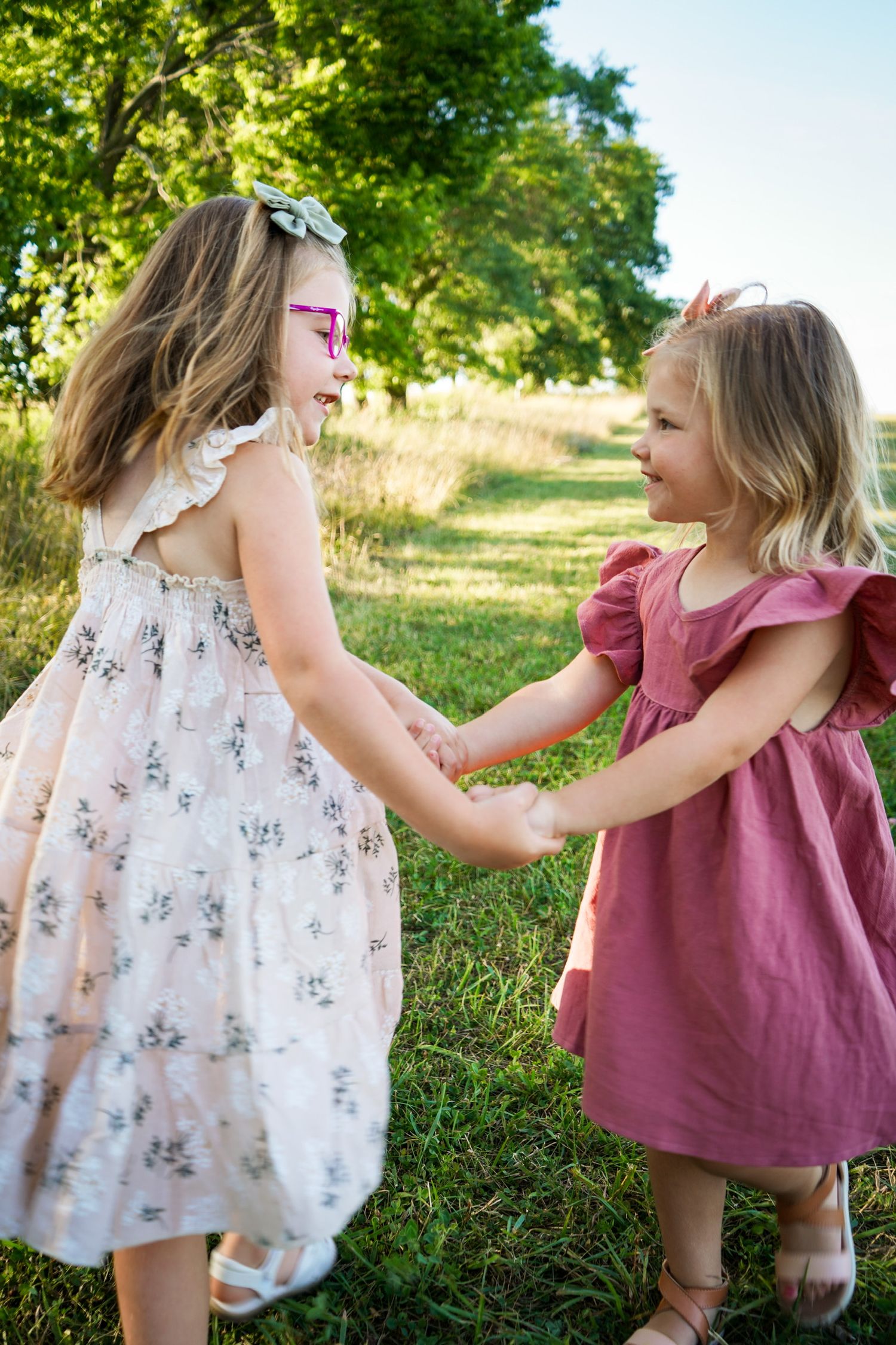 Two children in pretty dresses holding hands and playing in a sunny outdoor setting.