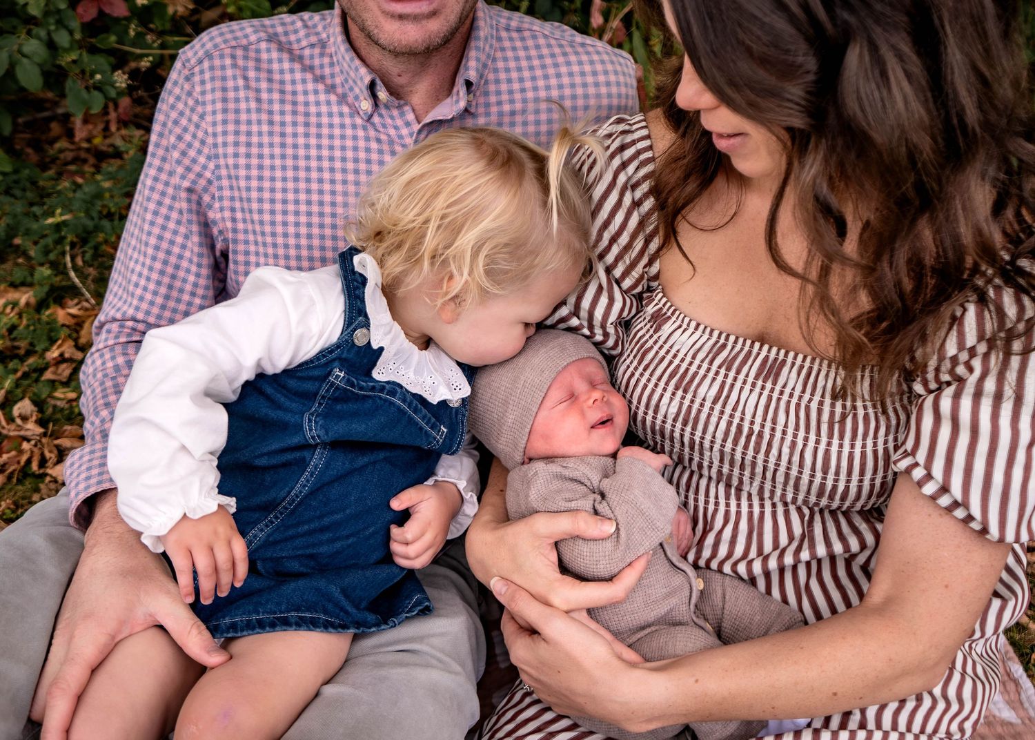 Family shares tender moments together on striped blanket in outdoor setting.