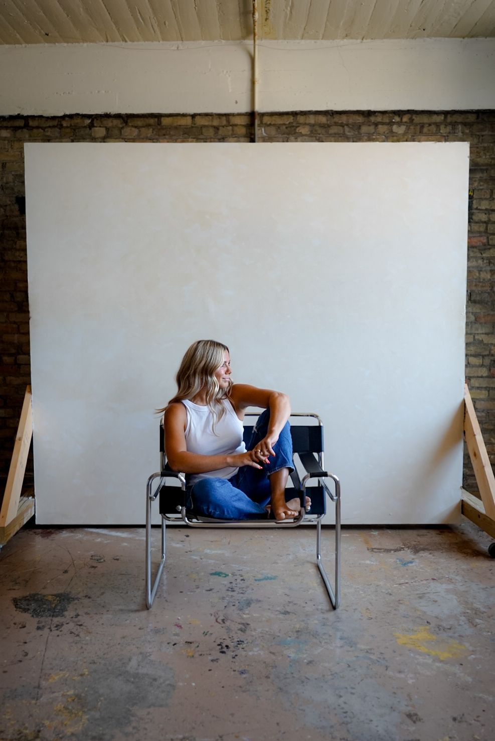 Person lying down on a bench in an empty room with white walls and exposed brick.
