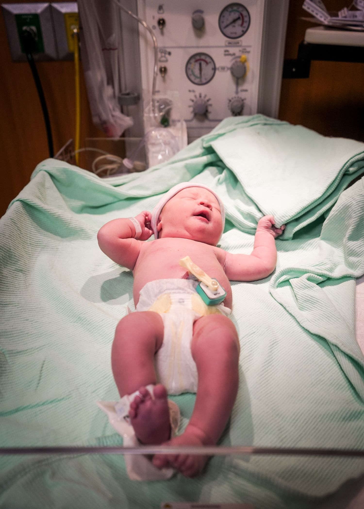 Newborn baby resting on medical bed with teal hospital linens.