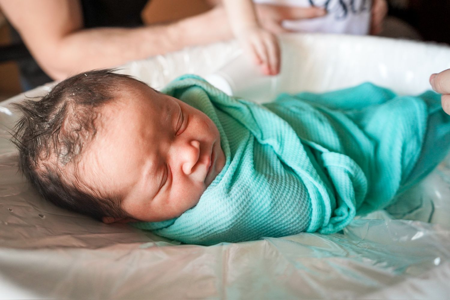 Side view of a peaceful newborn sleeping while wrapped in a mint green hospital swaddle.