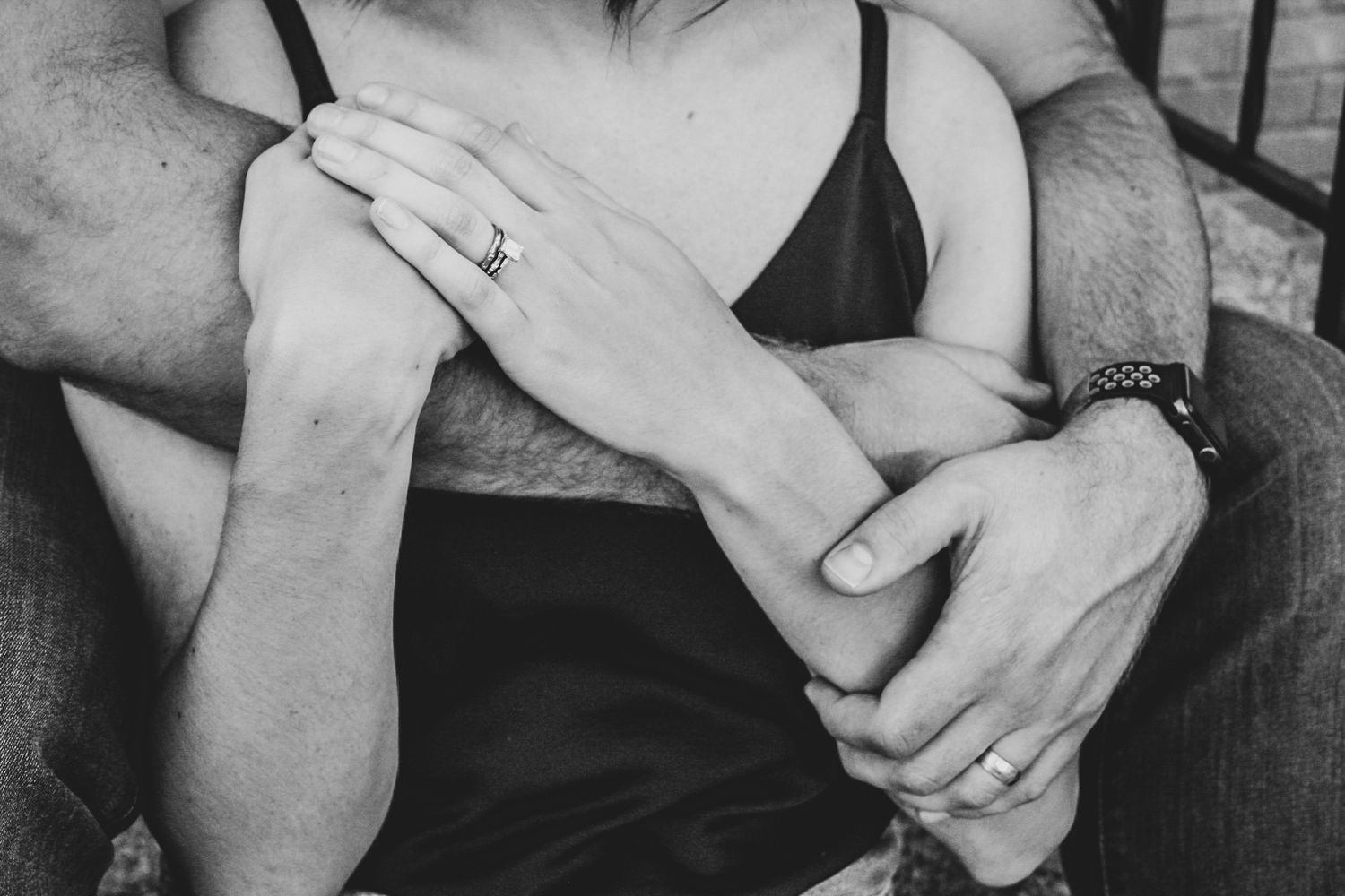A black and white close-up of two hands embracing intimately with a diamond ring visible.
