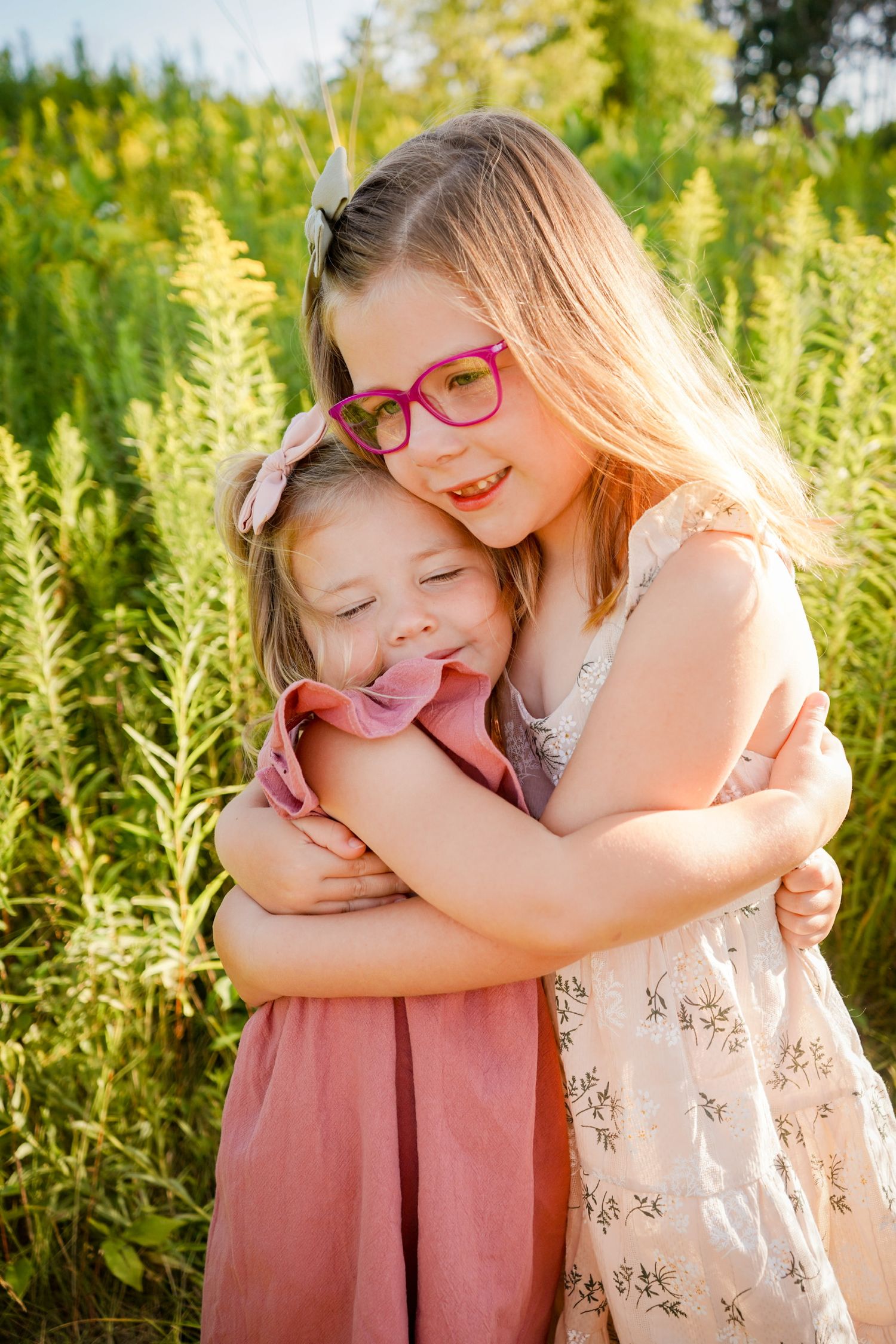 Two young friends hugging and laughing together in a field of tall yellow flowers.