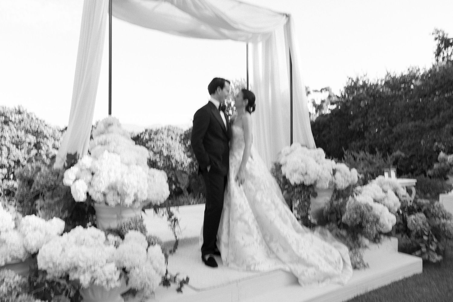 White floral decorations and fabric draping create an elegant outdoor wedding ceremony setting.