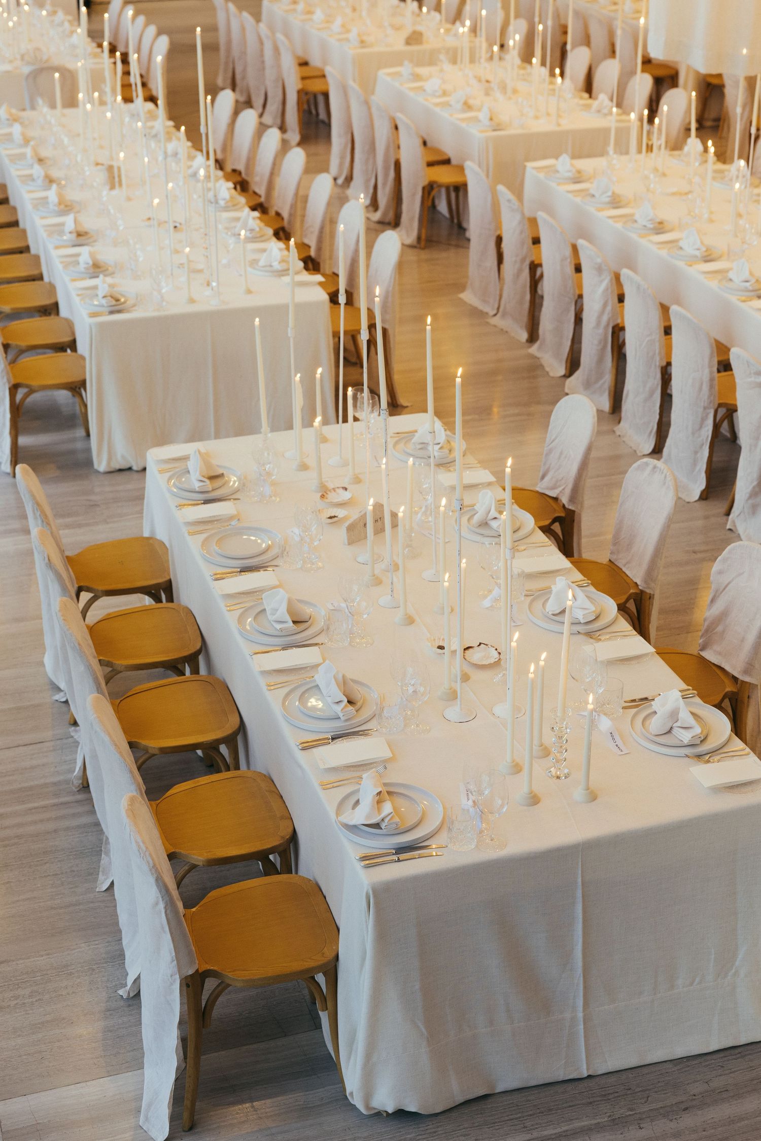 Elegant white banquet tables set for a formal event with white linens, tall candles, and gold chairs.