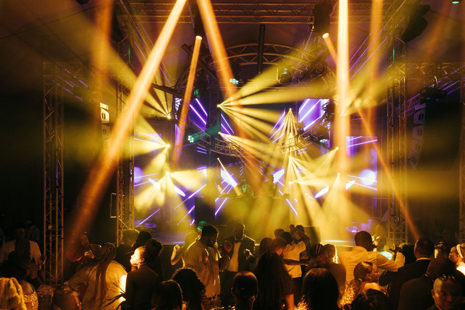 Golden spotlights and purple beams illuminate a crowded nightclub dance floor.