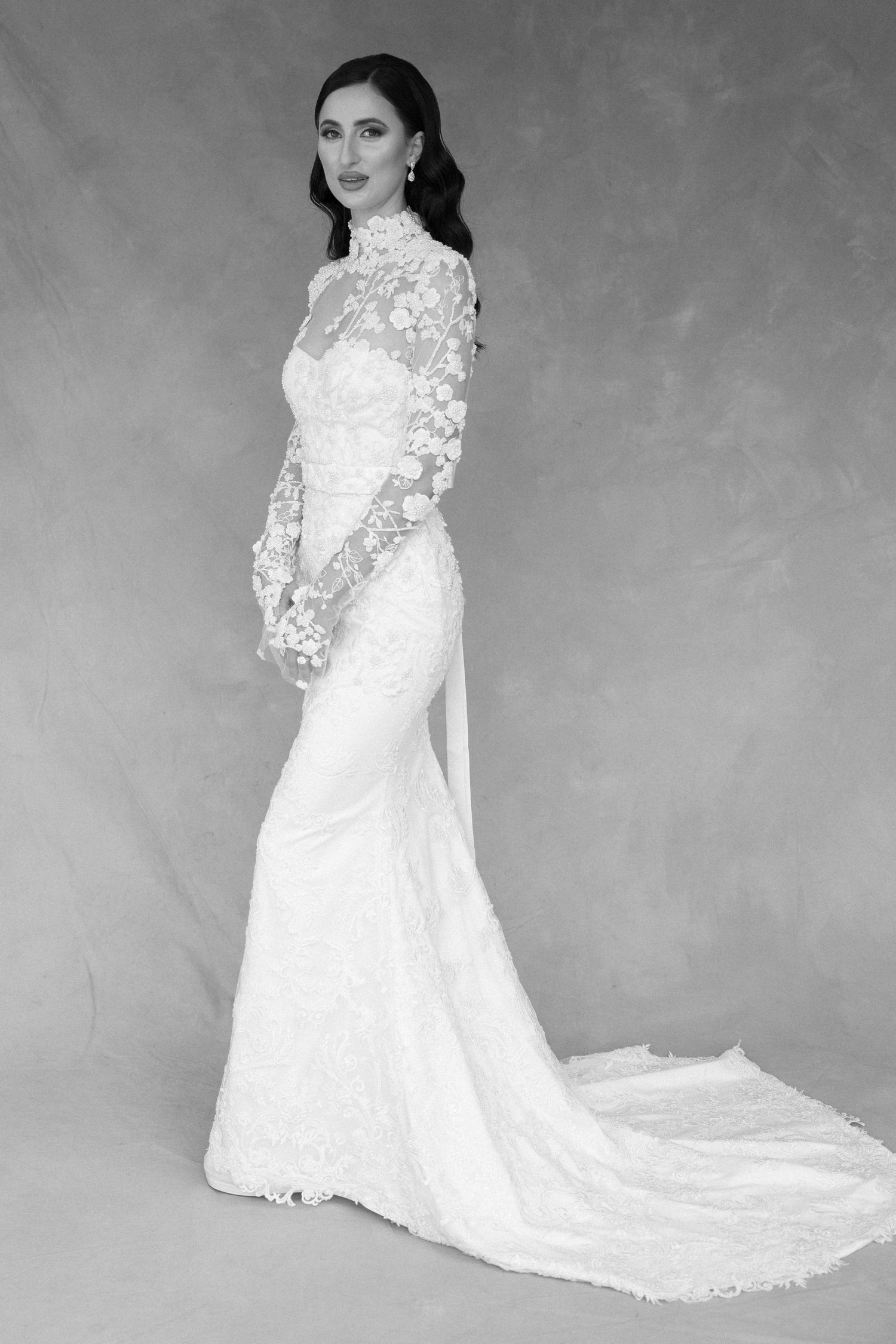 A lace-detailed white wedding gown with long sleeves and a flowing train in black and white.