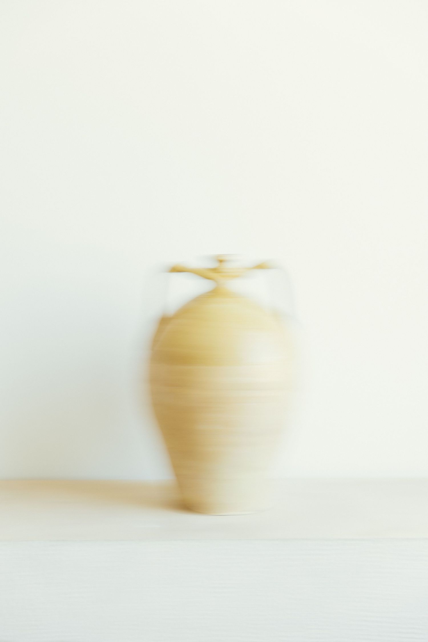 A soft focus artistic photograph of a beige ceramic vase against a white background.