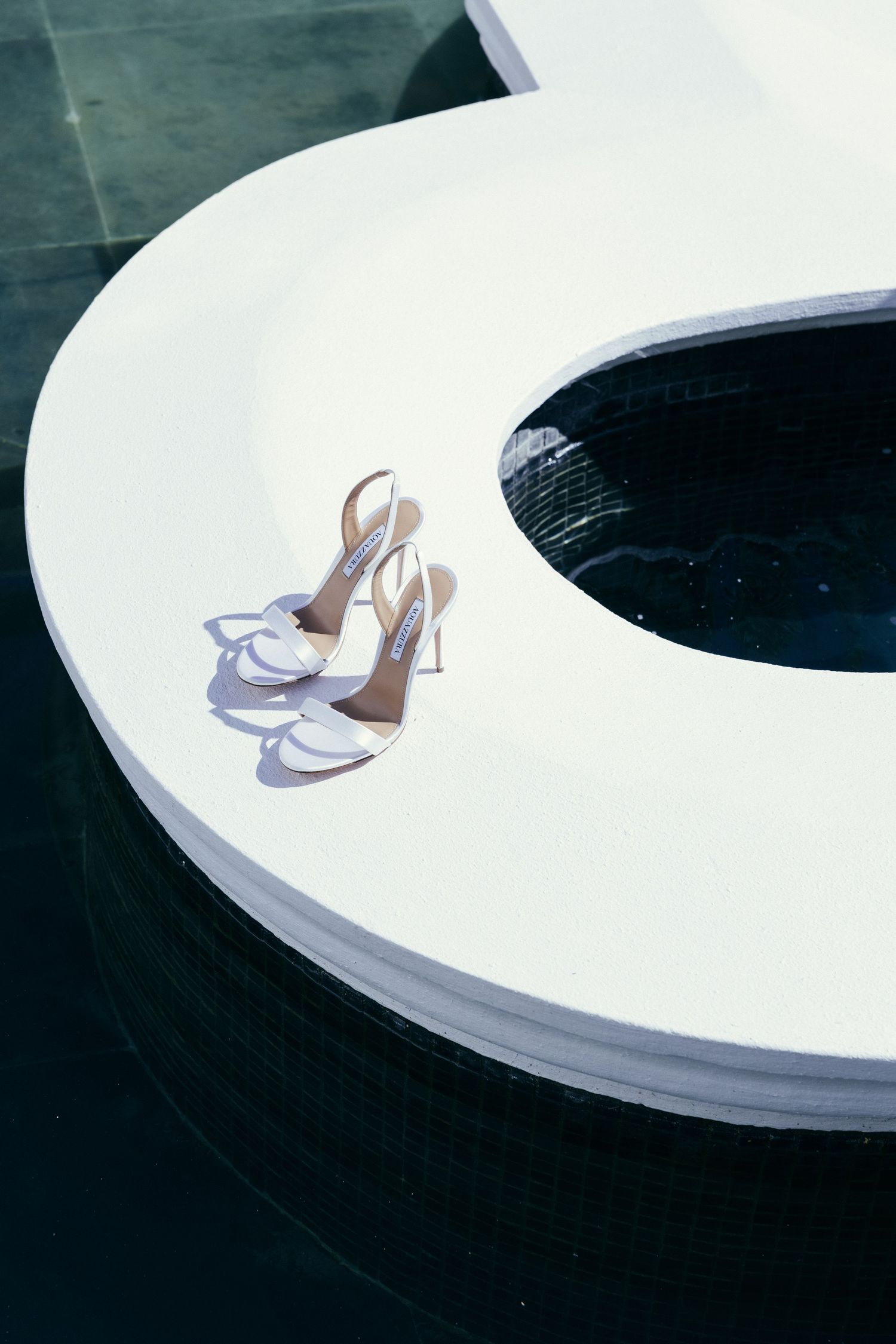 White high heel bridal shoes placed on a curved white surface against a dark background.