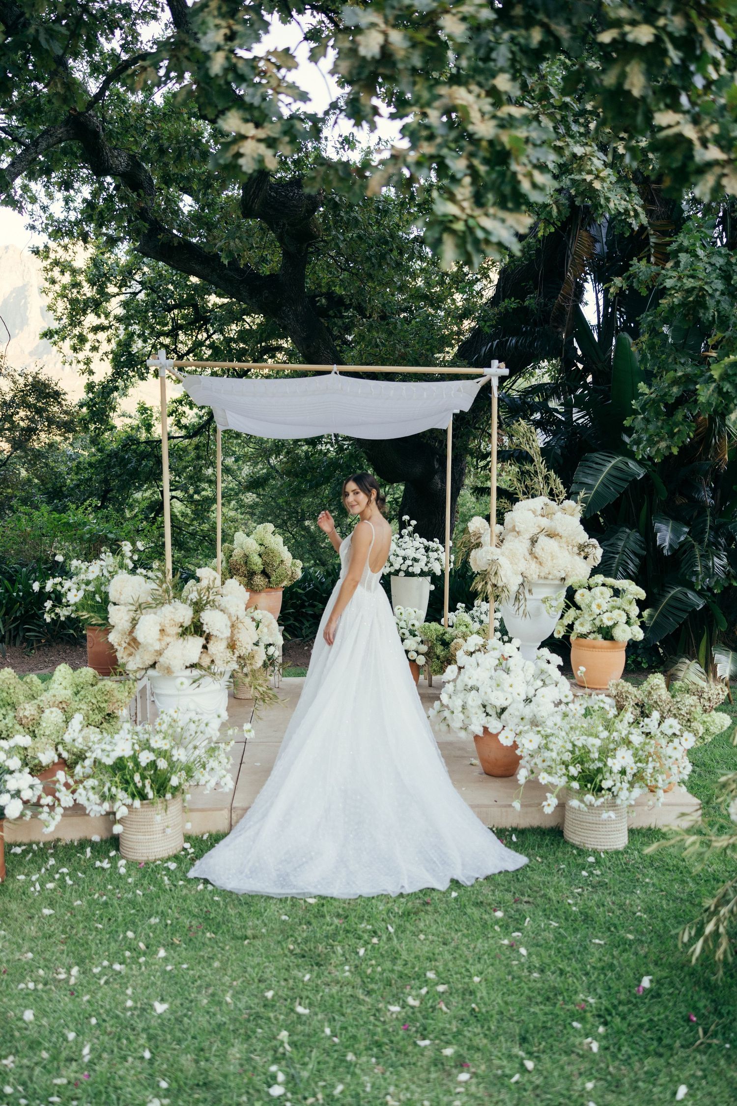 Garden wedding setup with white canopy and floral arrangements surrounding an elegant gown.