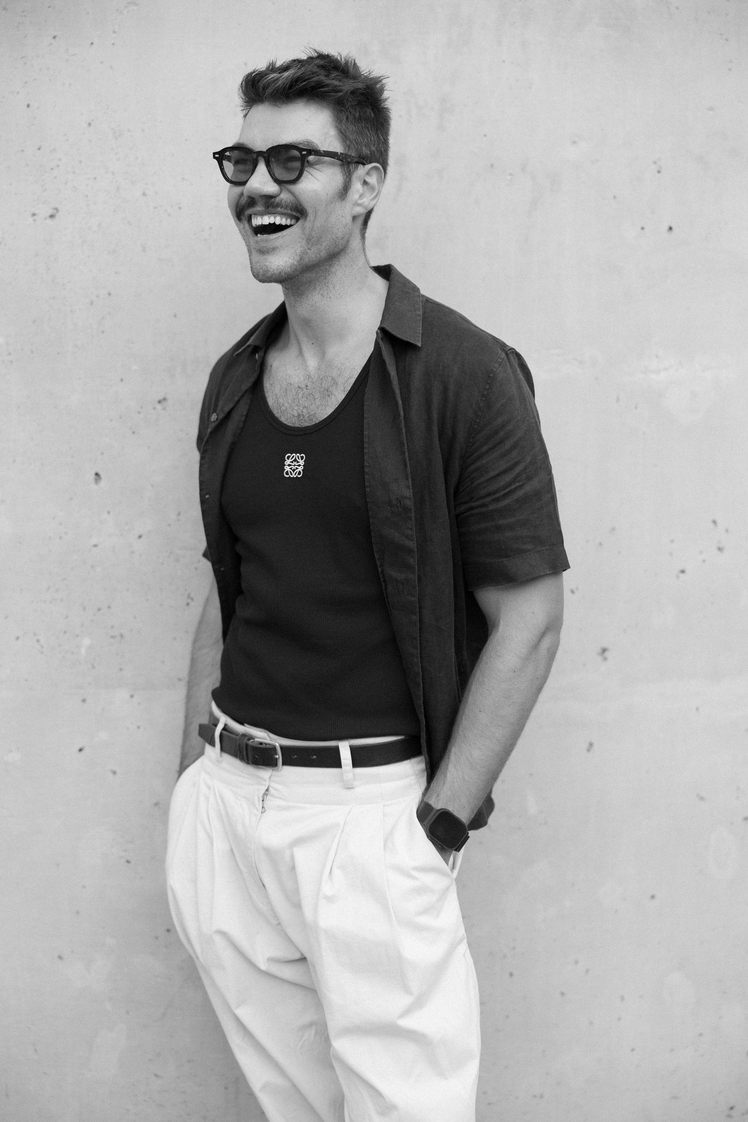 A stylish black and white portrait series showing a person in a casual black top and white pants against a wall.