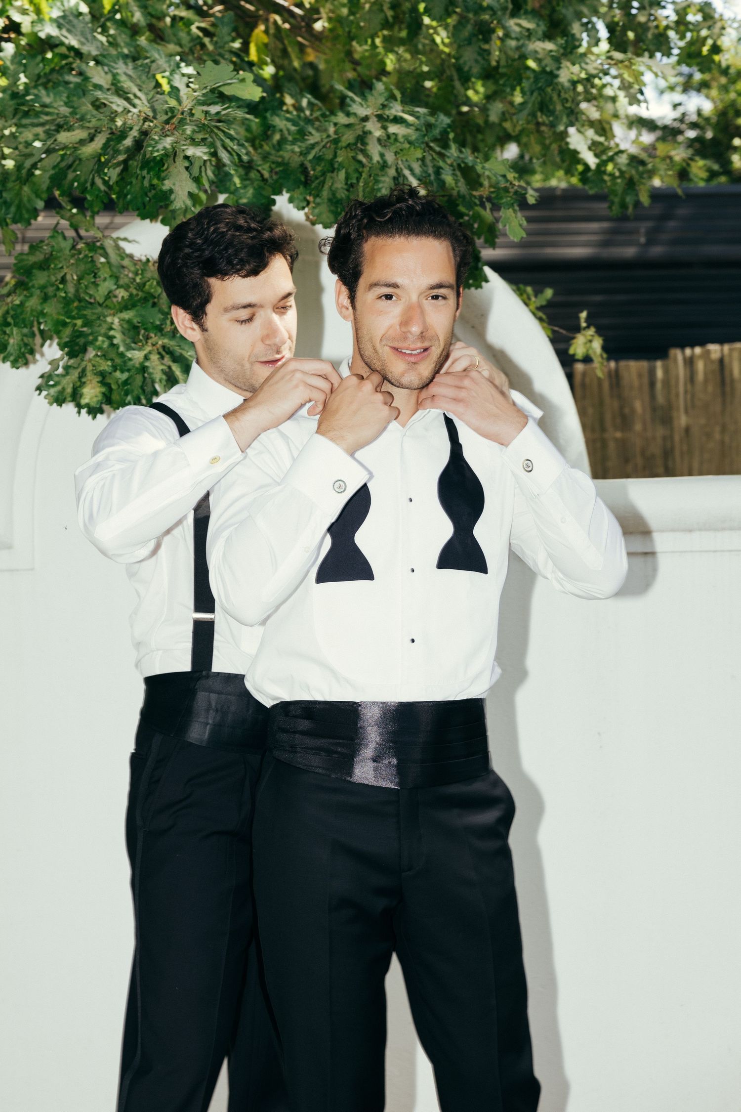Group wearing formal black and white attire posing together under green foliage.