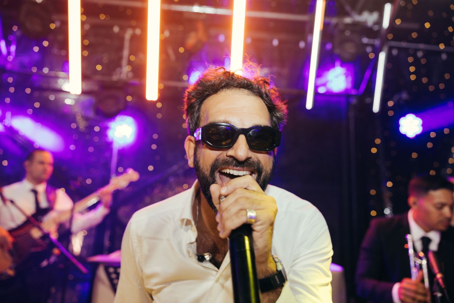 Performer singing on stage with sunglasses under colorful purple and orange lighting effects.