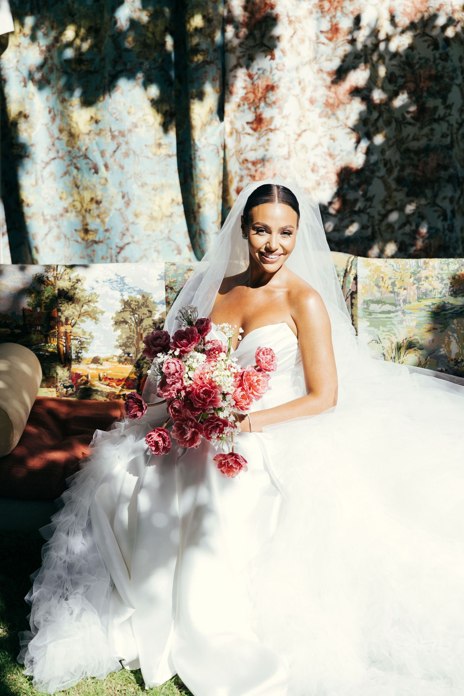 A stunning outdoor bridal portrait featuring a white wedding gown and vibrant pink bouquet against a textured backdrop.