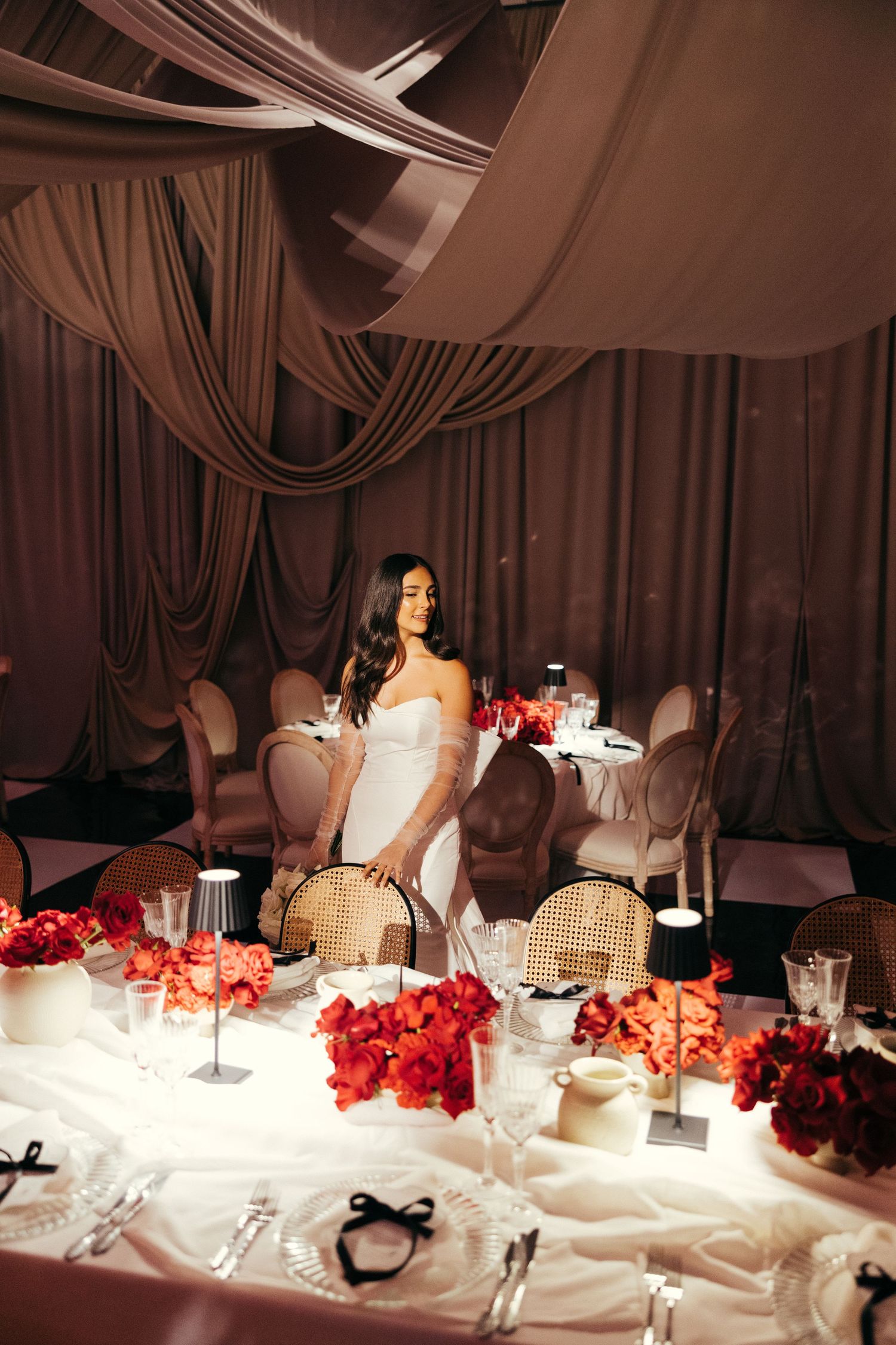 Elegant wedding reception table with pink flowers and draped fabric decor overhead.