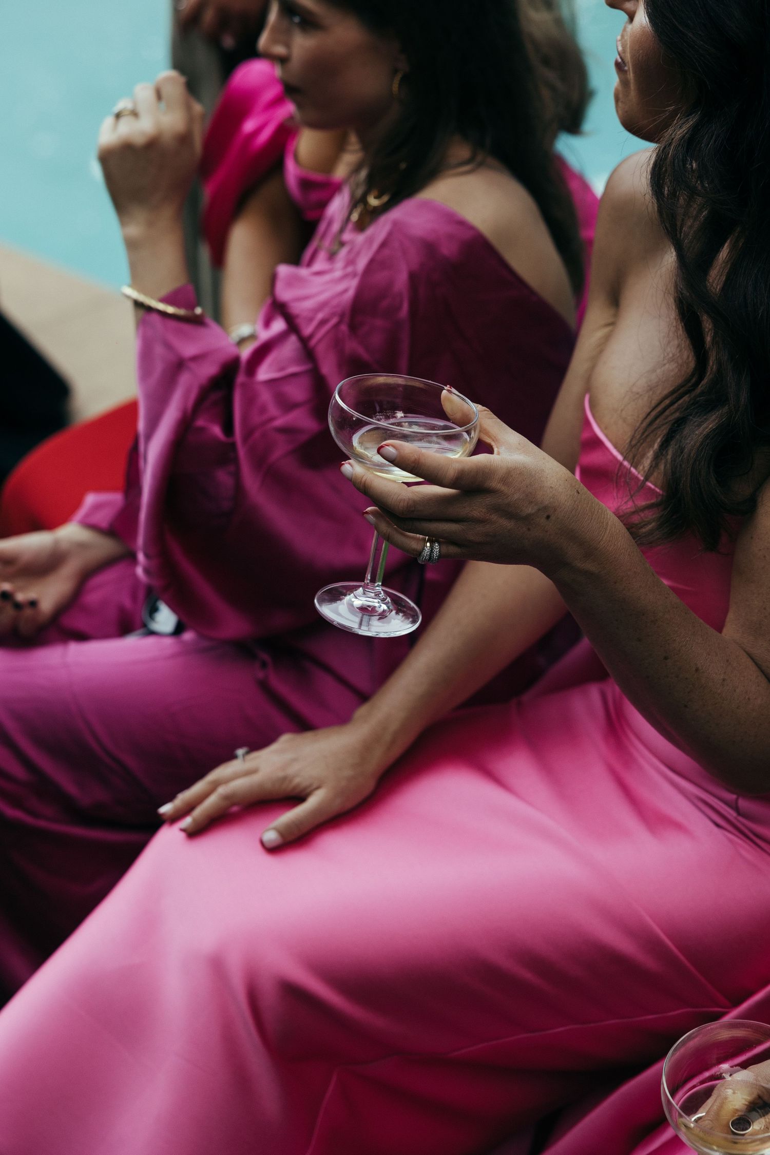 Bridesmaids in vibrant pink dresses hold wine glasses during wedding celebration.