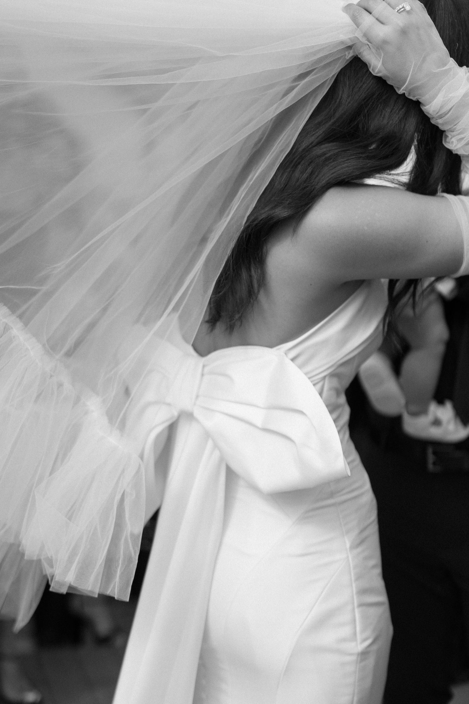 Close-up black and white photo of bride adjusting her flowing white tulle veil.
