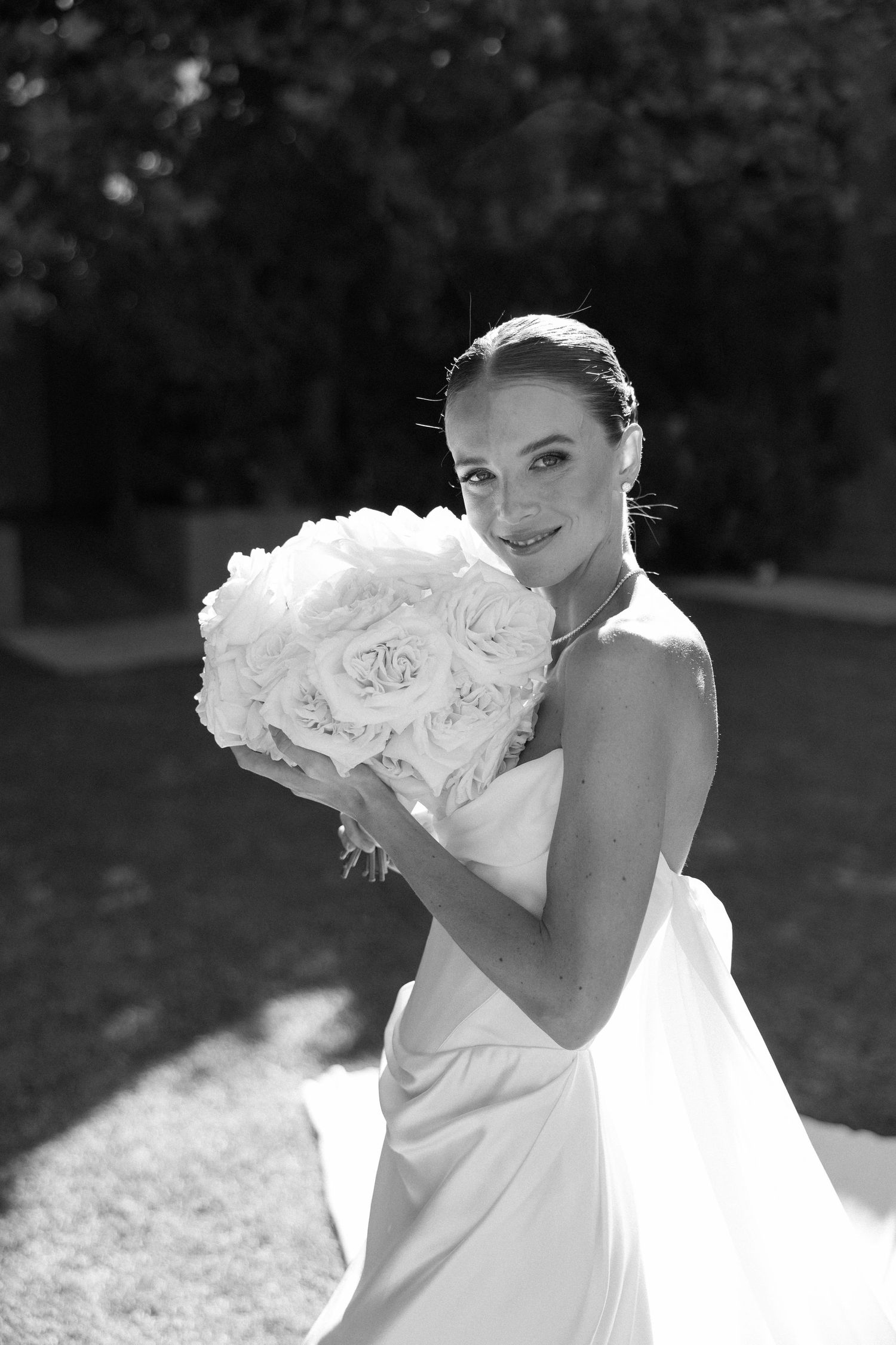 Elegant black and white bridal portrait with white roses outdoors in sunlight.