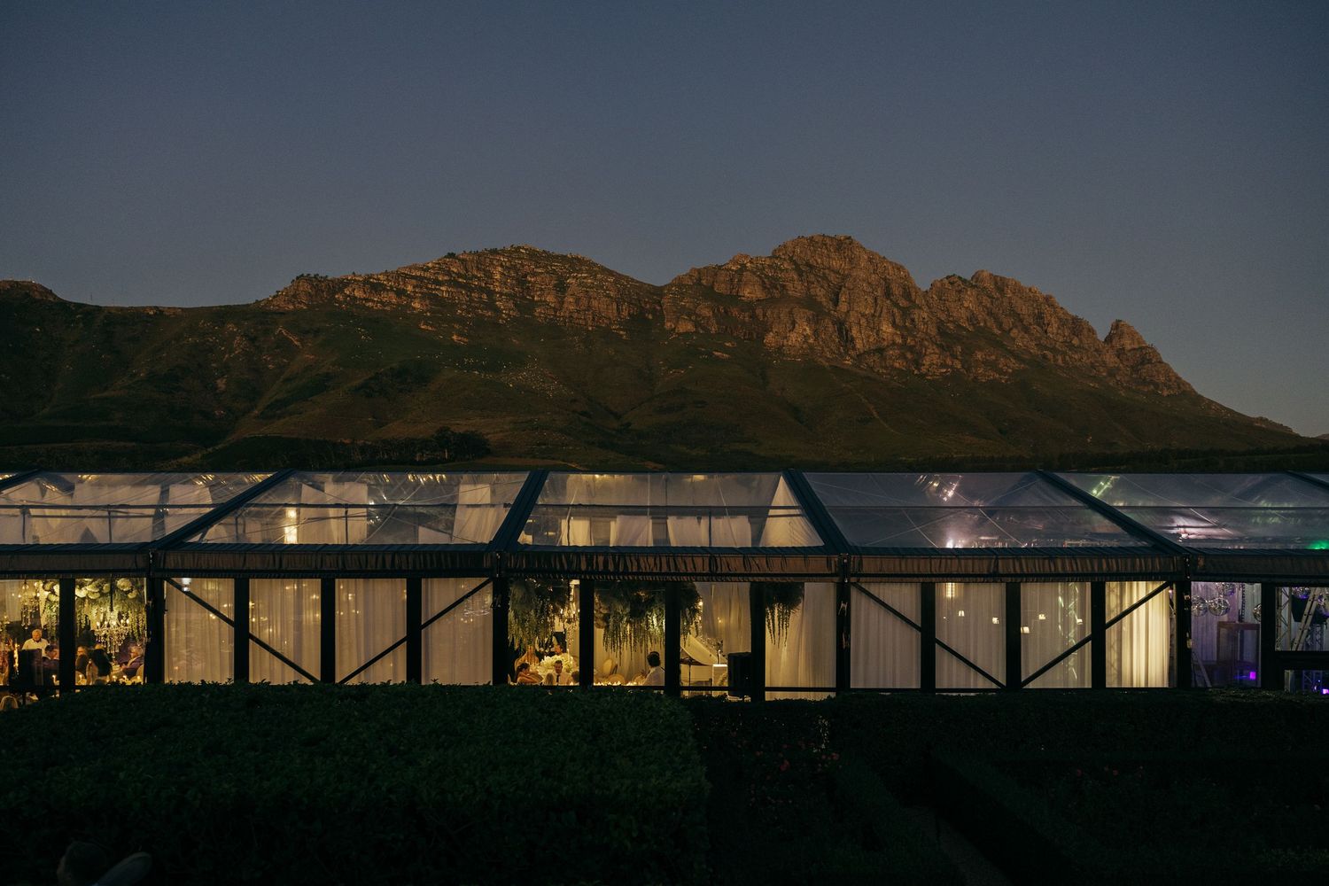 Glass-walled reception venue at dusk with mountain backdrop.
