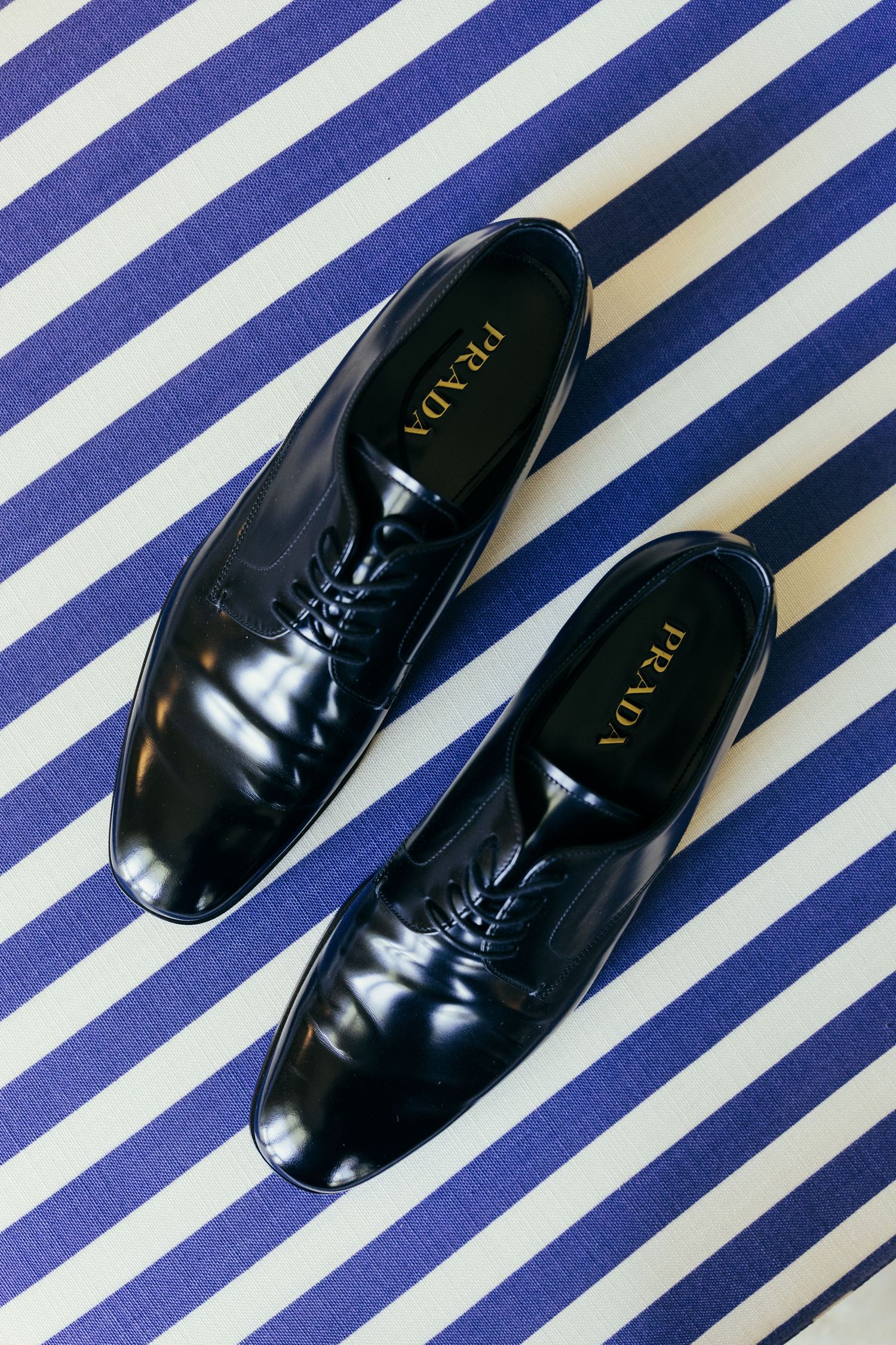 Shiny black formal men's dress shoes on a blue and white striped fabric background.