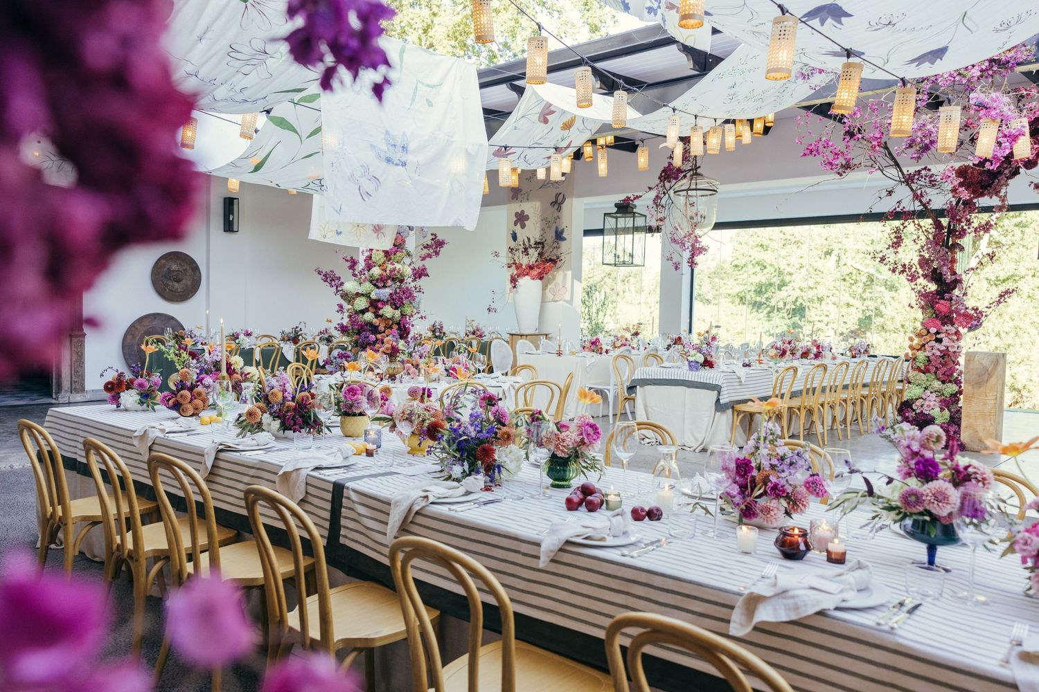 Elegant wedding table setup with purple floral arrangements and gold chairs in a bright venue.