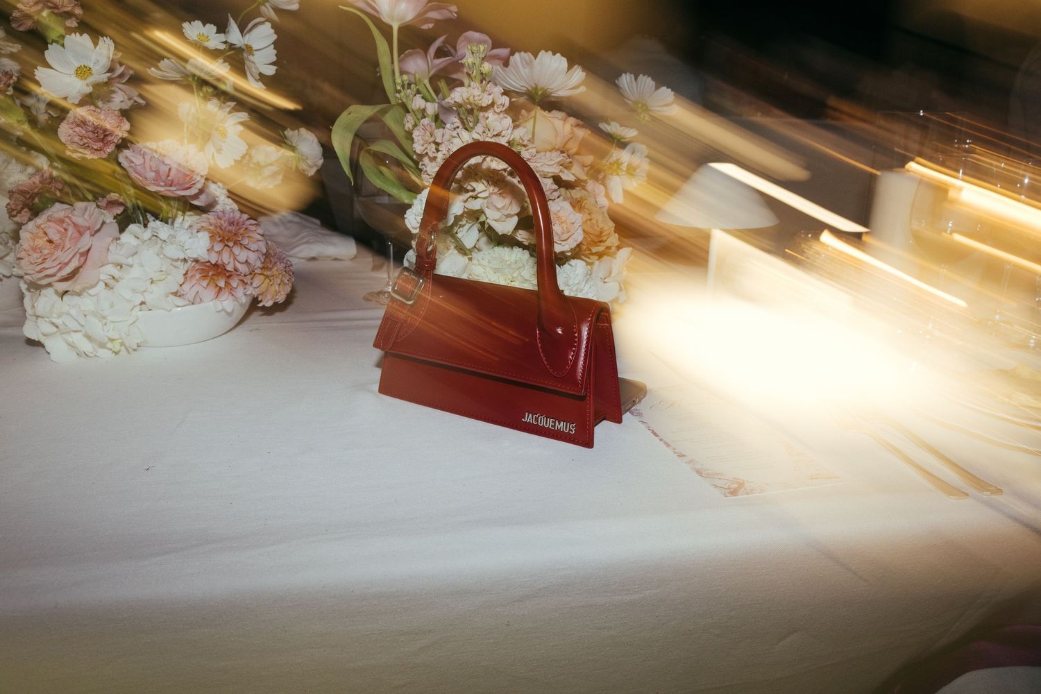 A red designer handbag sits on a white surface with soft pink roses in the background.