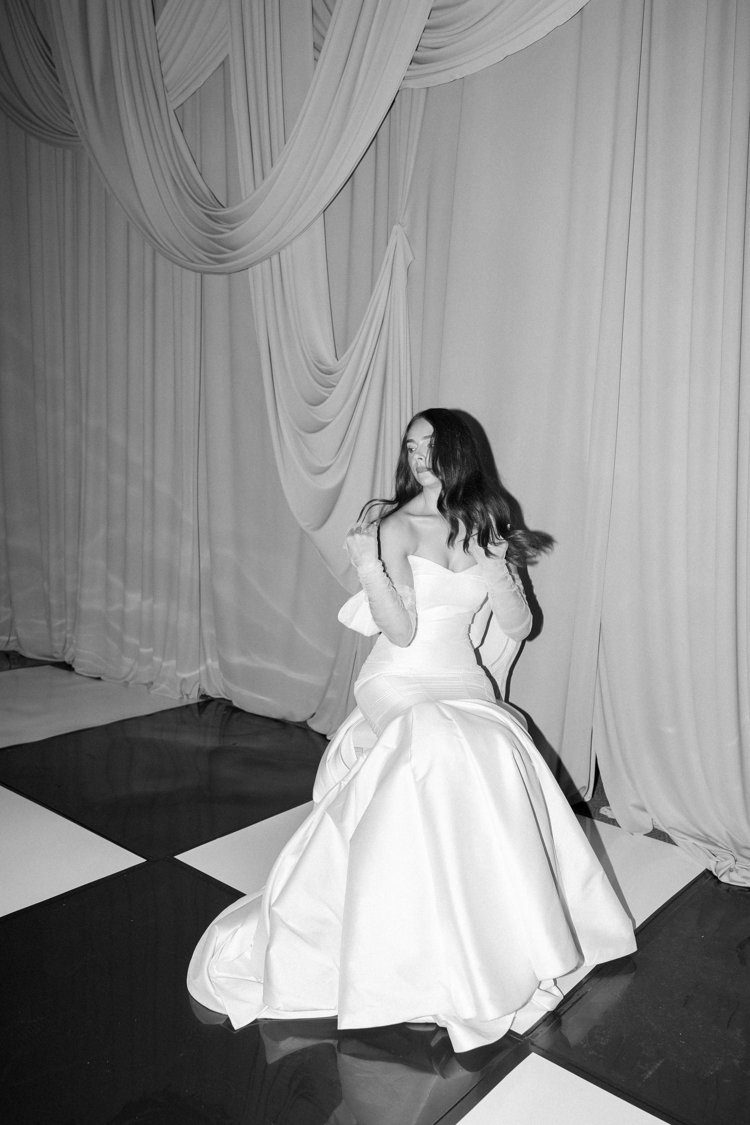 Black and white photo of bride in strapless ballgown against white draped backdrop.