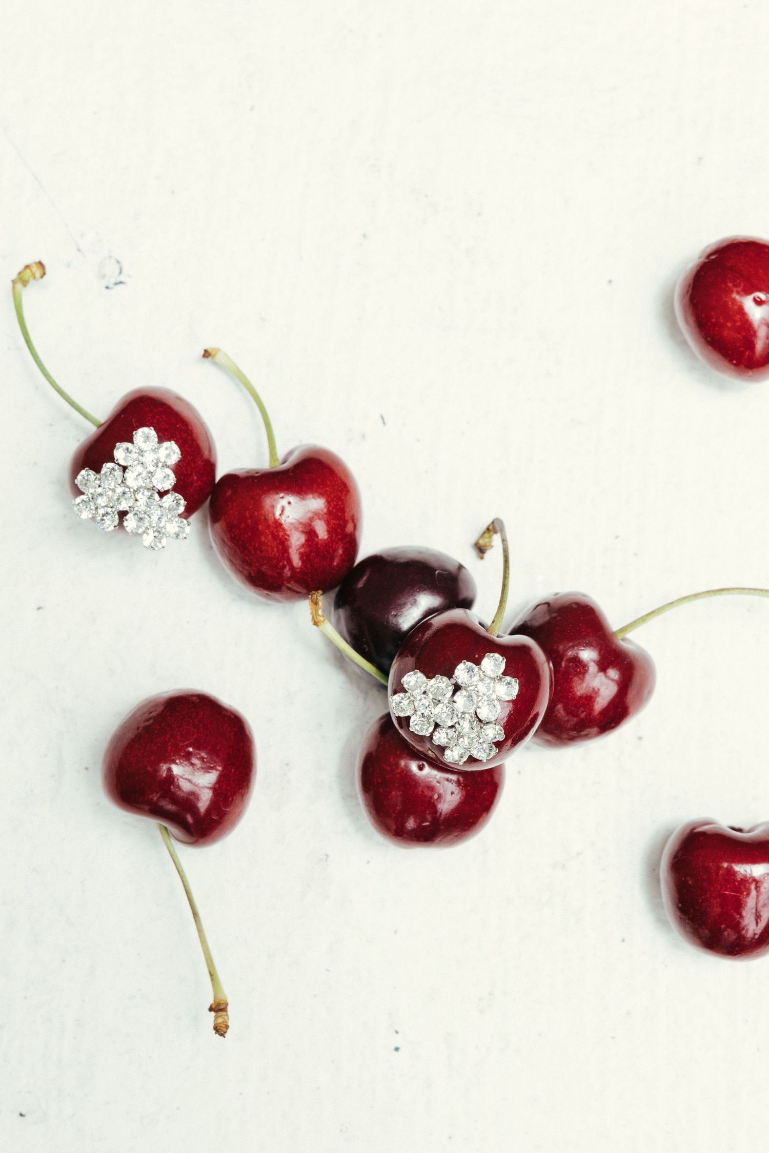 Fresh red cherries arranged with delicate crystal jewelry decorations on a white background.