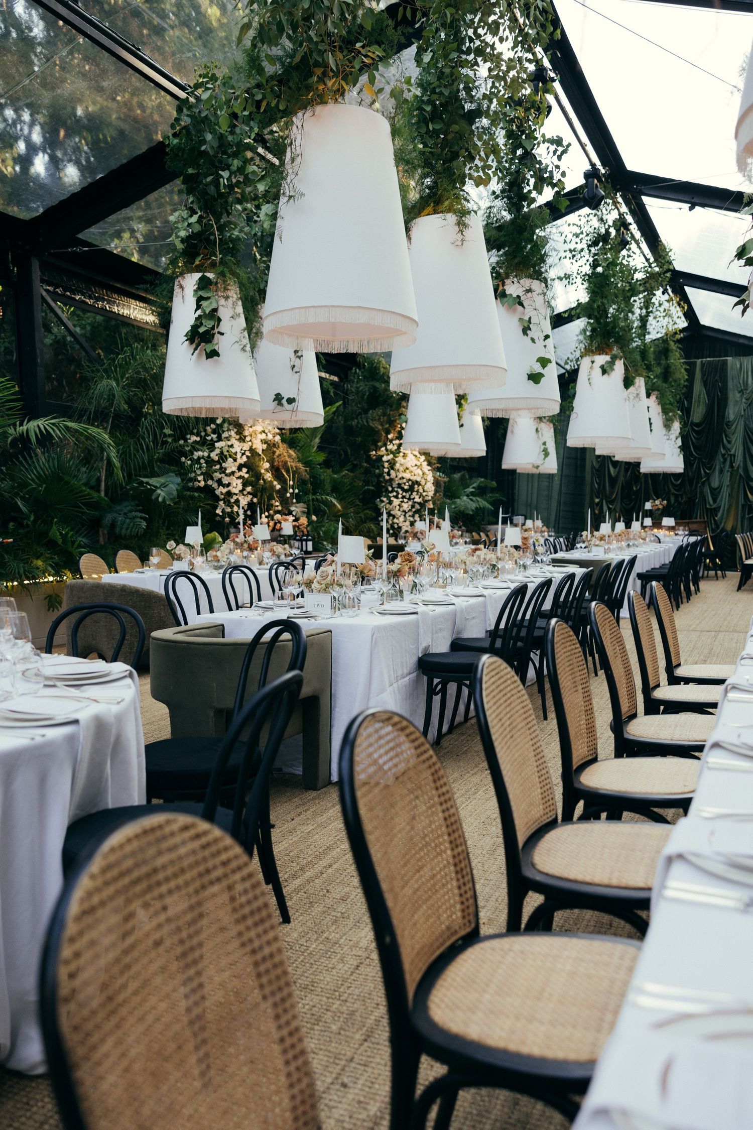 Elegant wedding reception setup with woven chairs and white tablecloths under hanging pendant lights.