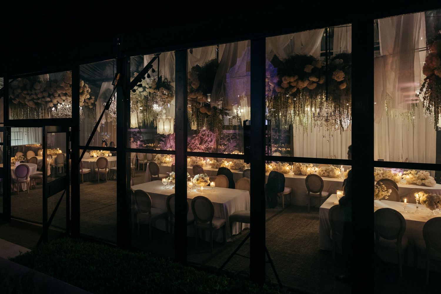 Evening view through windows of an illuminated wedding reception venue.