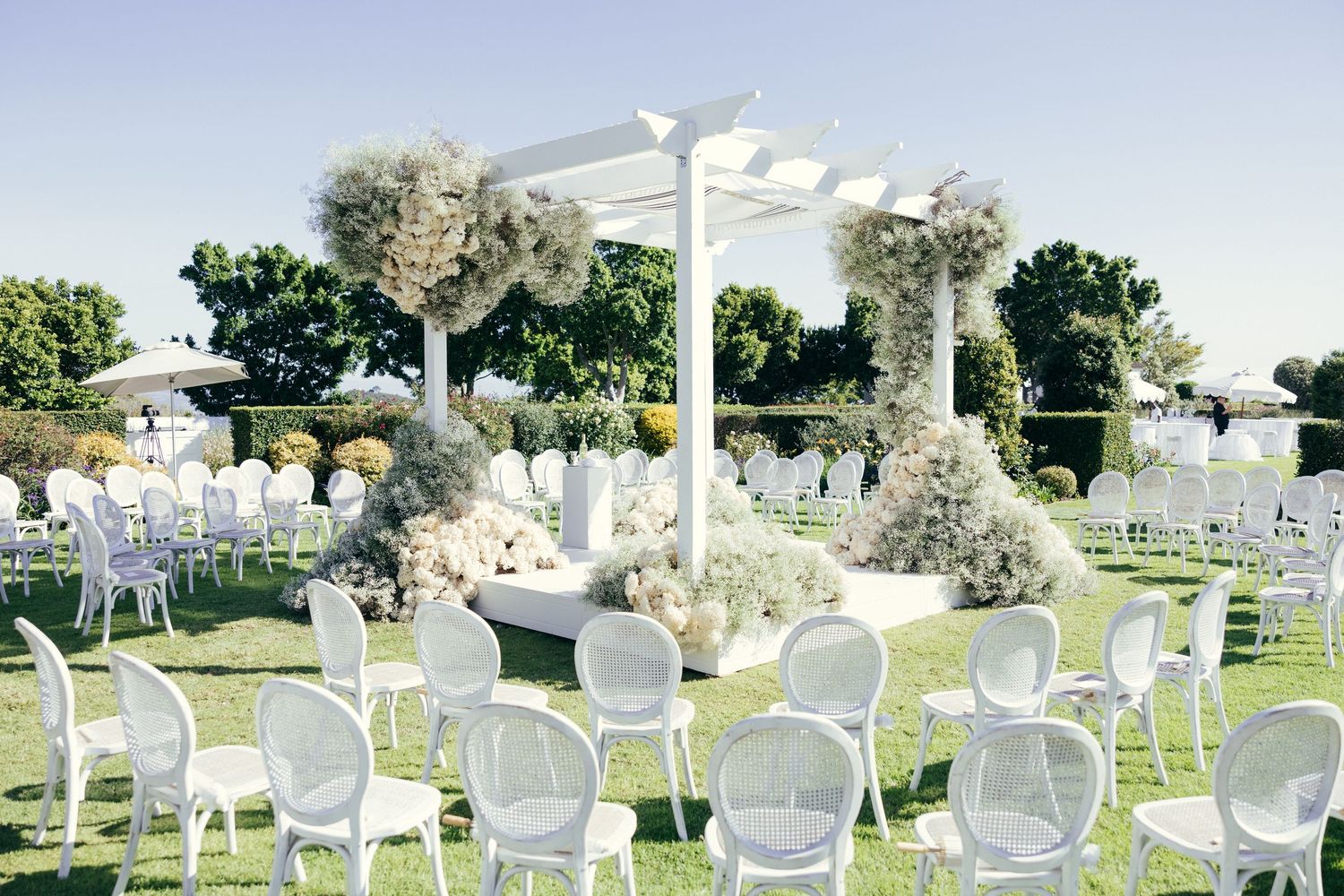 White garden chairs arranged in rows for outdoor ceremony with floral decorations.