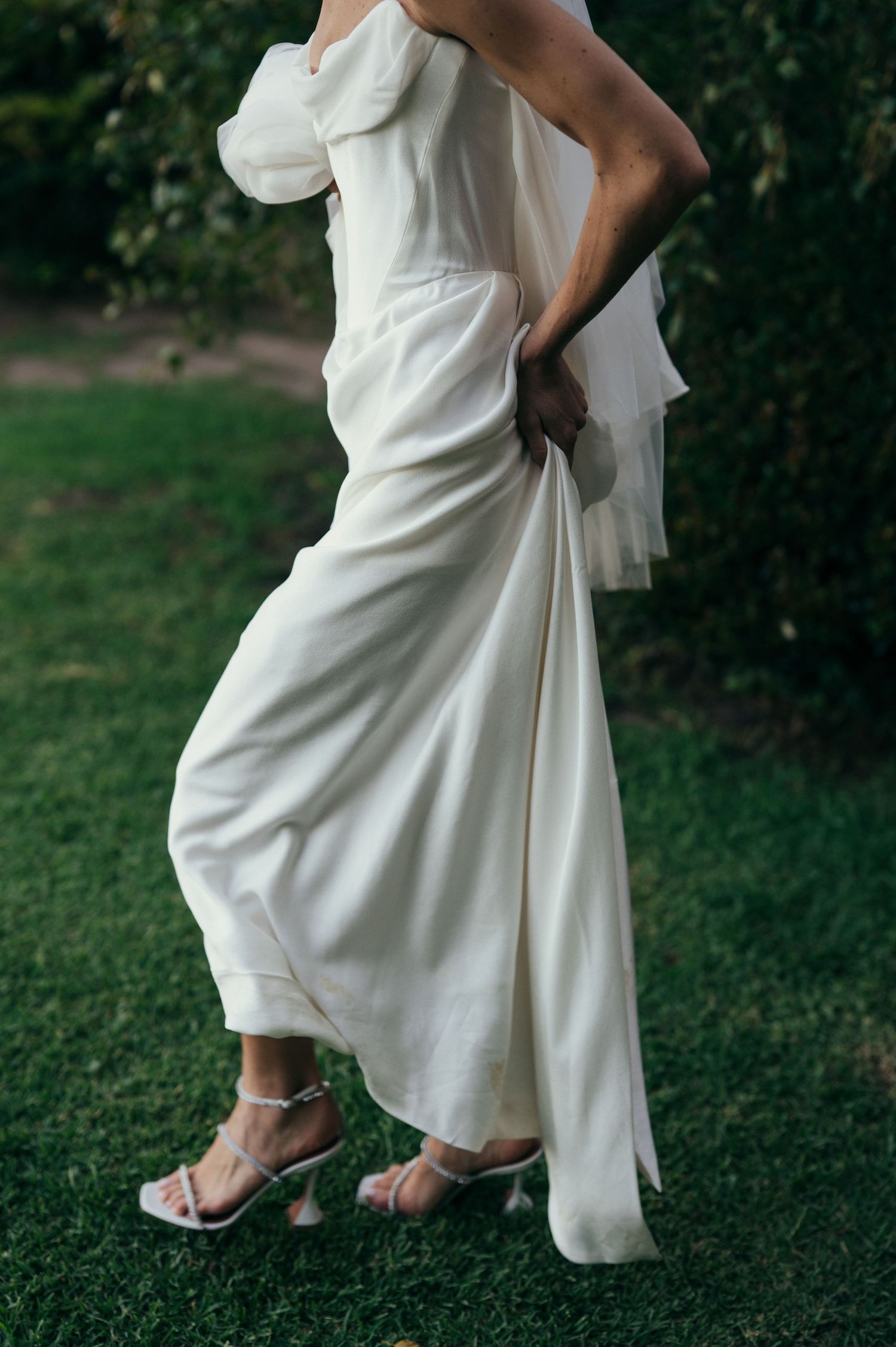 White wedding dress detail showing hemline and sandals on grass.