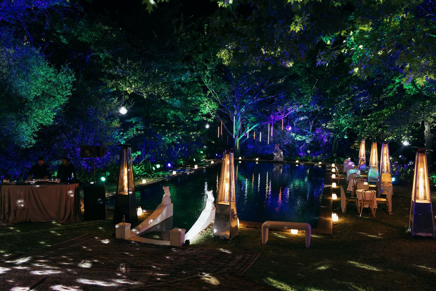 Enchanting outdoor wedding reception setup illuminated by blue lighting and lanterns under trees at night.