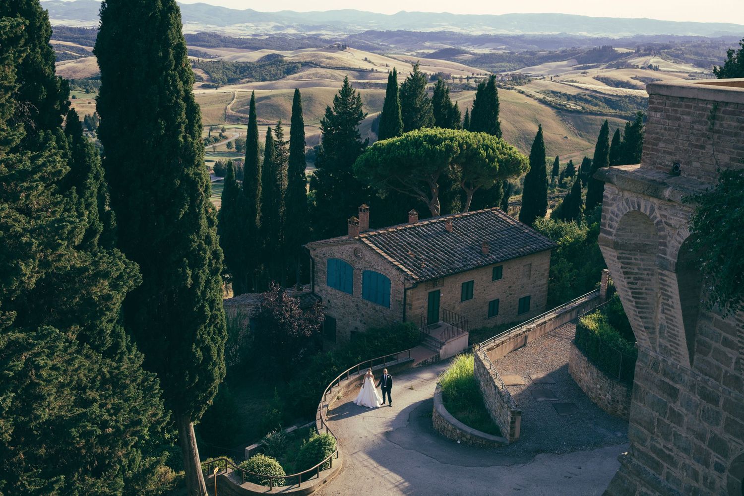 Aerial view of a rustic Tuscan villa surrounded by cypress trees and rolling hills with a wedding couple.