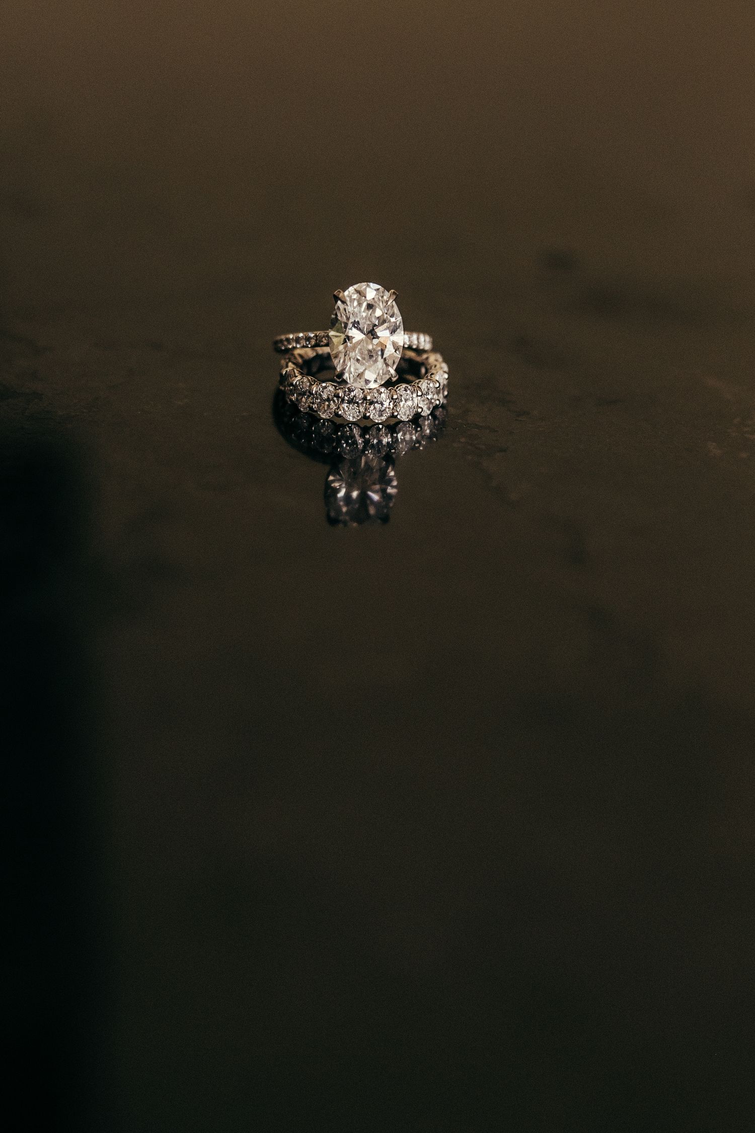 Sparkling diamond engagement ring with ornate design photographed on dark surface.