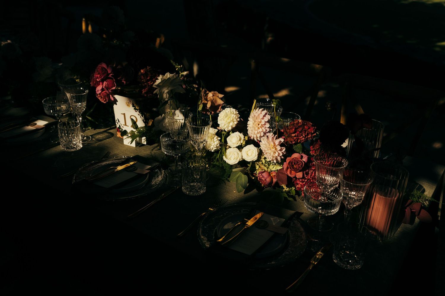 Moody evening table setting with candlelight and dark floral arrangements.