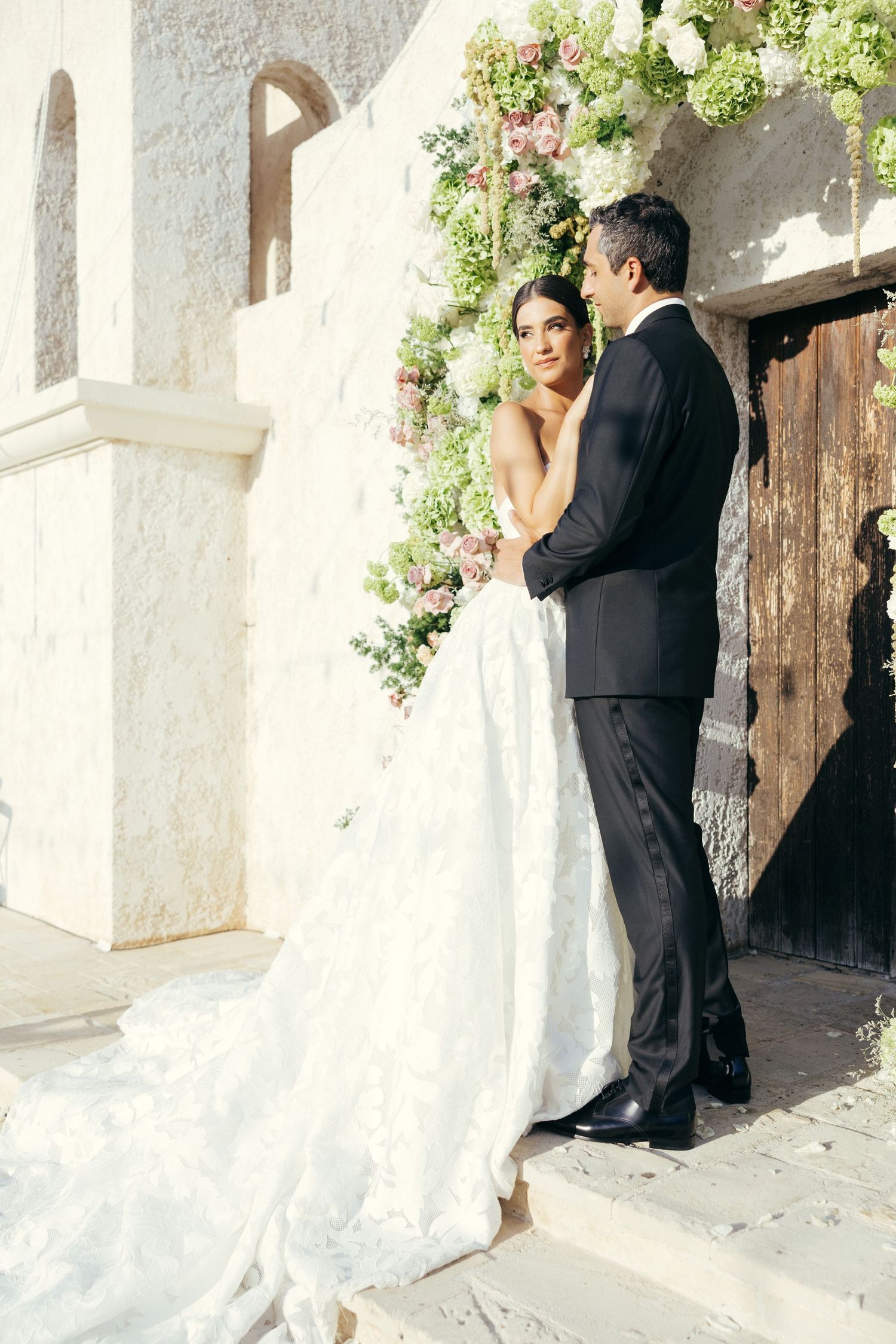 A romantic moment outside a Mediterranean white building adorned with flowers.