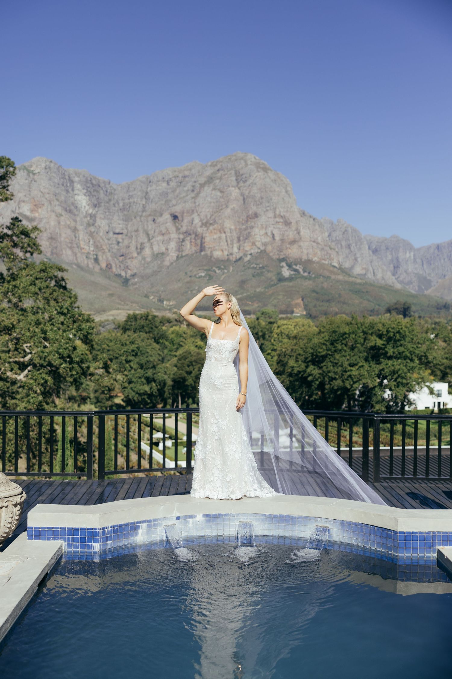 A wedding dress silhouette against mountain scenery and blue pool reflection.