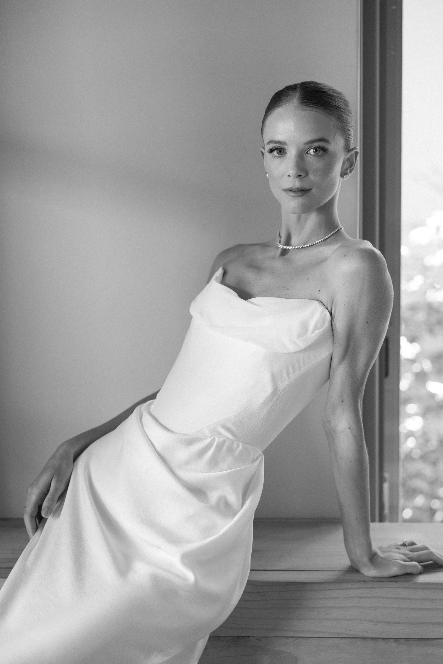 Artistic black and white portrait showing flowing white fabric against a window in natural light.