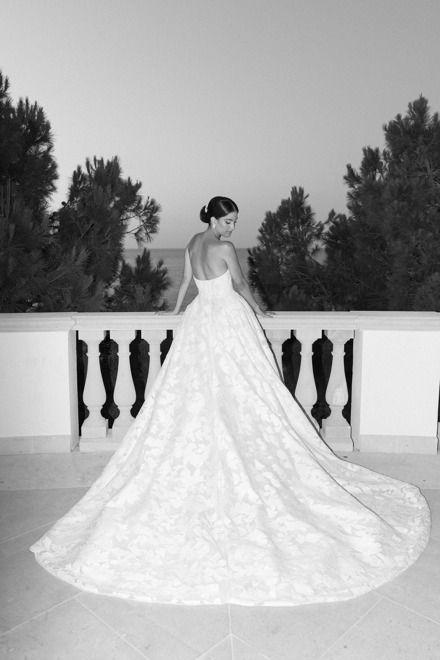 A dramatic black and white photo of a flowing wedding gown with a long train on a balcony.