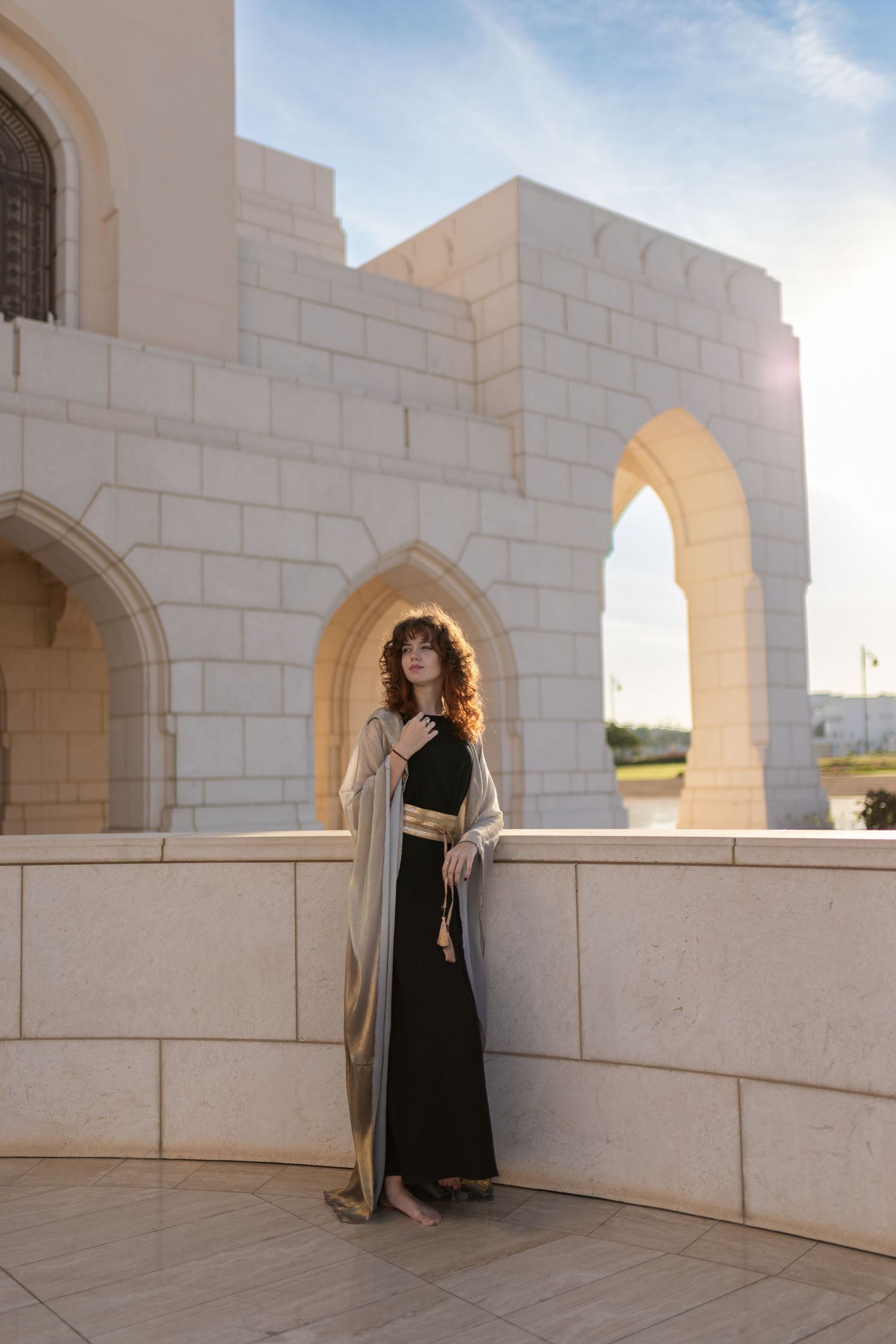 Two figures in black dresses stand in a white stone archway at sunset creating dramatic silhouettes.