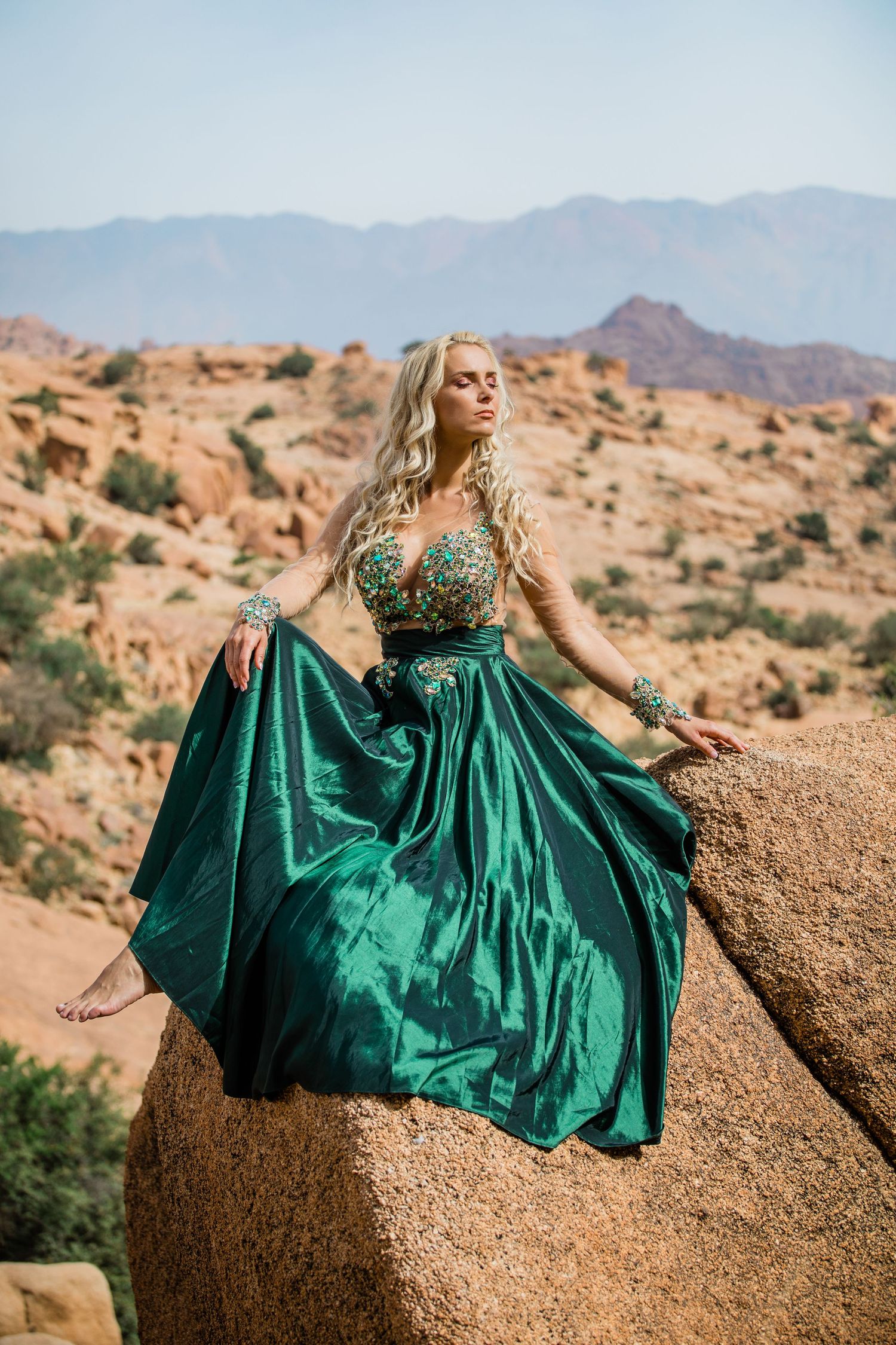 A flowing emerald green dress contrasts beautifully against red rock formations in a desert landscape.