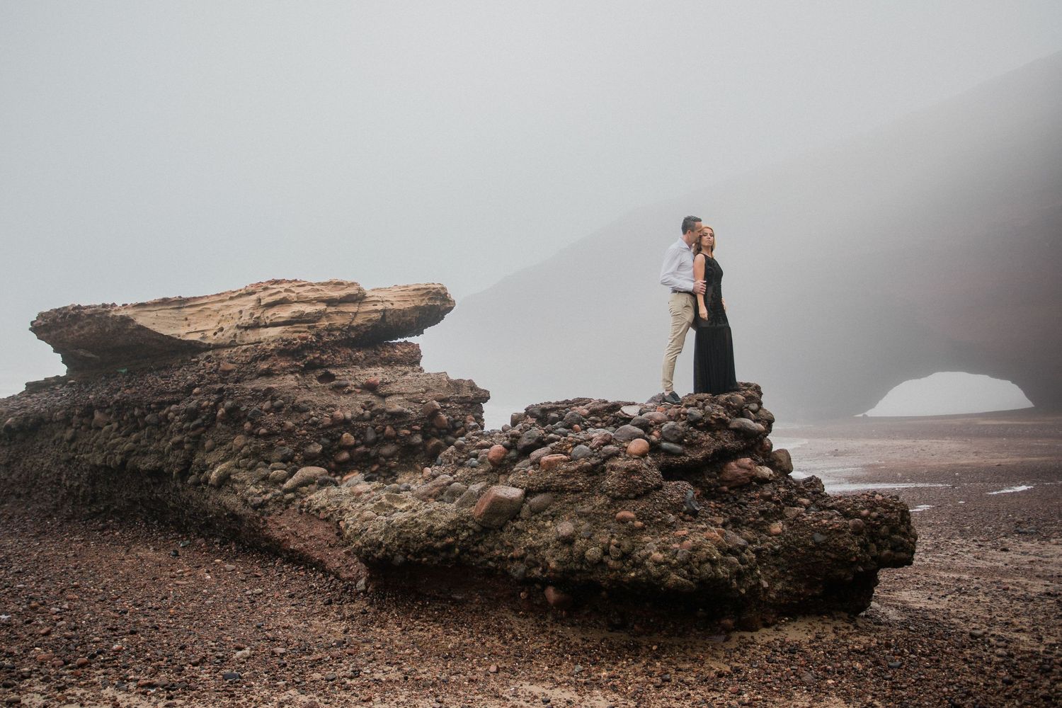 A rocky coastal landscape with large boulders and misty atmosphere along a foggy beach.