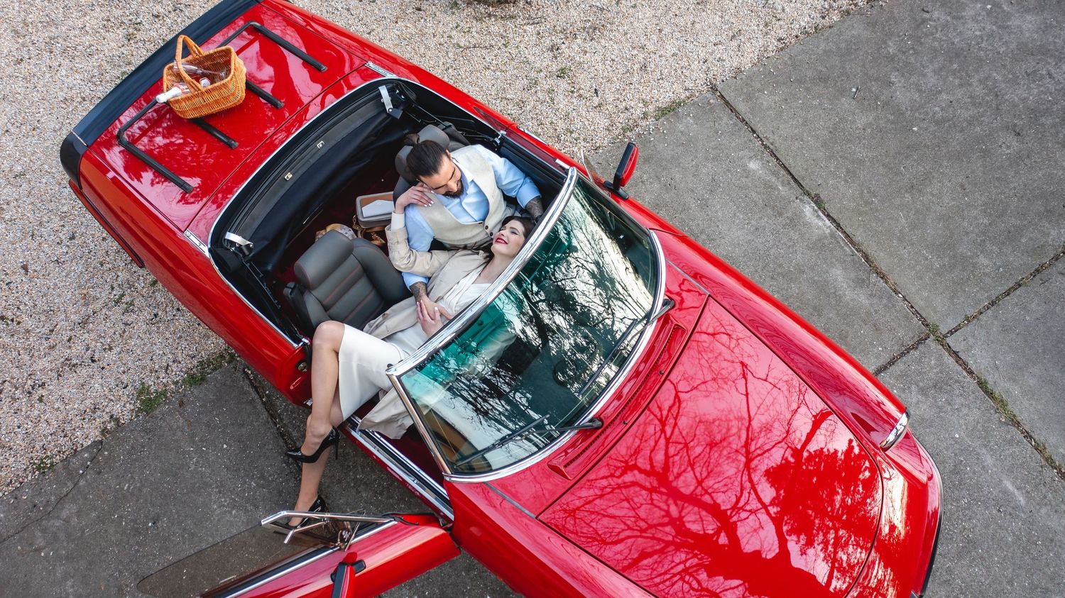 Aerial view of a shiny red vintage convertible car parked on a street with someone relaxing in the driver's seat.